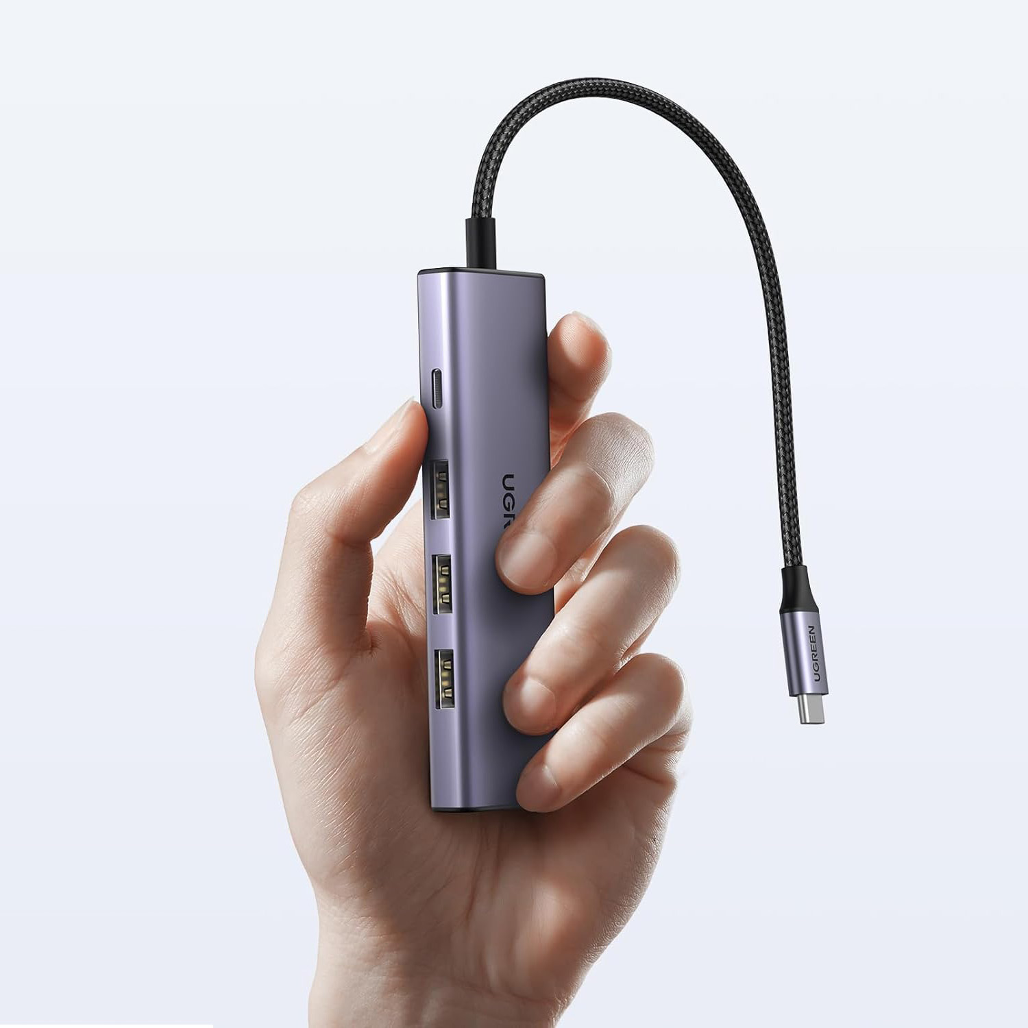 Bir el, çoklu bağlantı noktalarına ve bağlı bir kabloya sahip mor bir UGREEN USB-C hub'ı tutuyor.