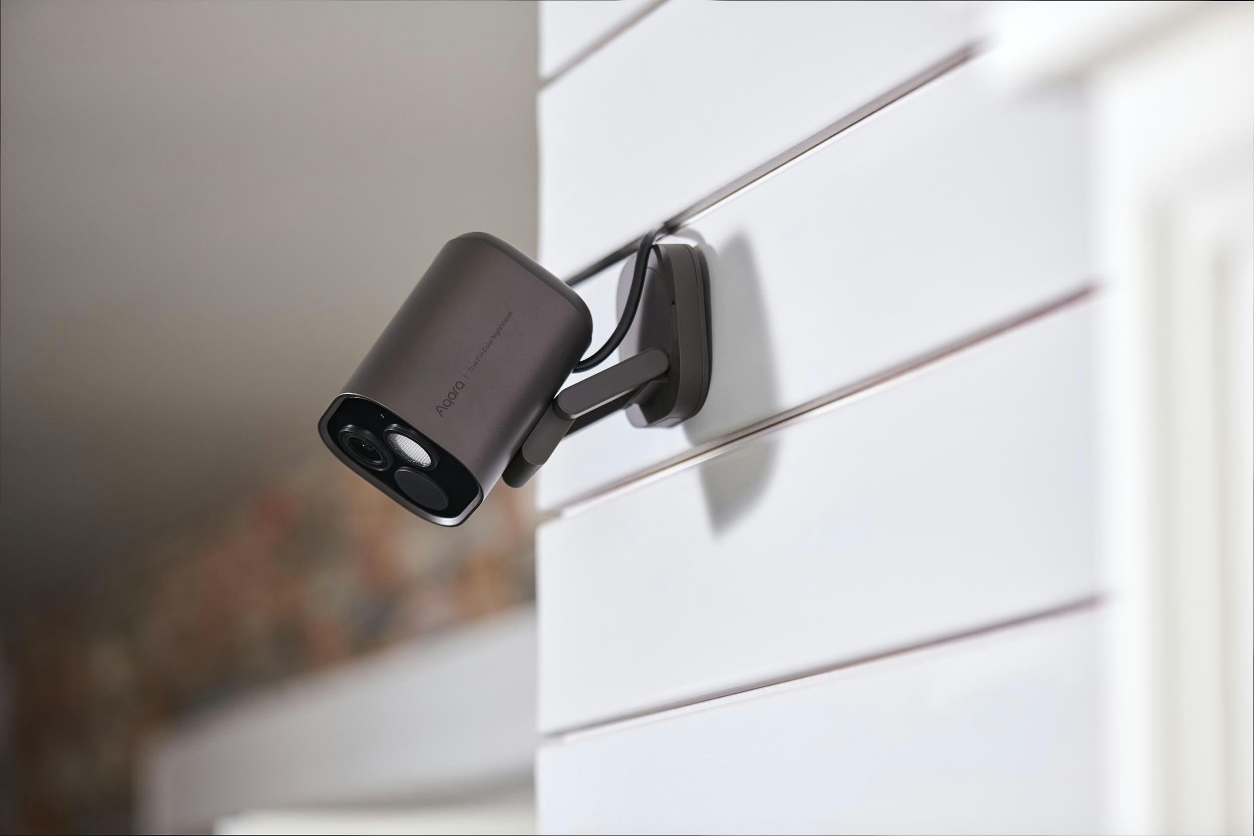 Dunkelgraue Überwachungskamera an einer weißen, horizontal gestreiften Wand.