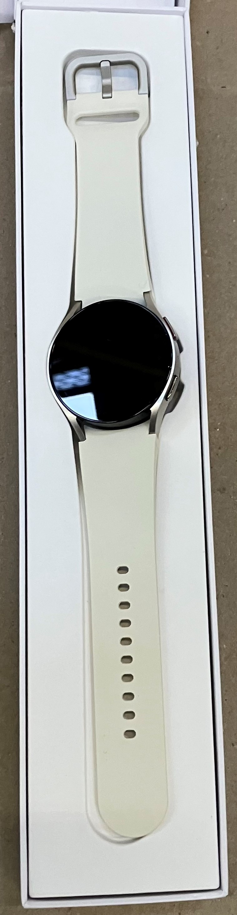 Biały smartwatch z czarnym wyświetlaczem leży w białym pudełku.