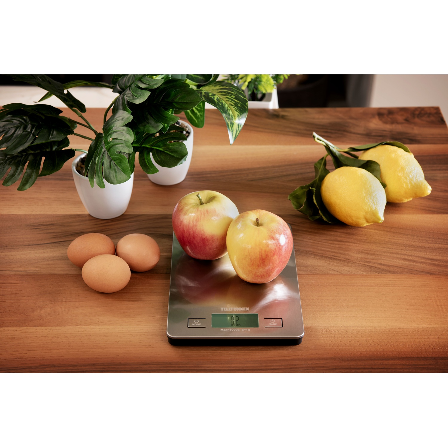 Bilancia da cucina con mele, limoni e uova su una superficie di legno, con piante.