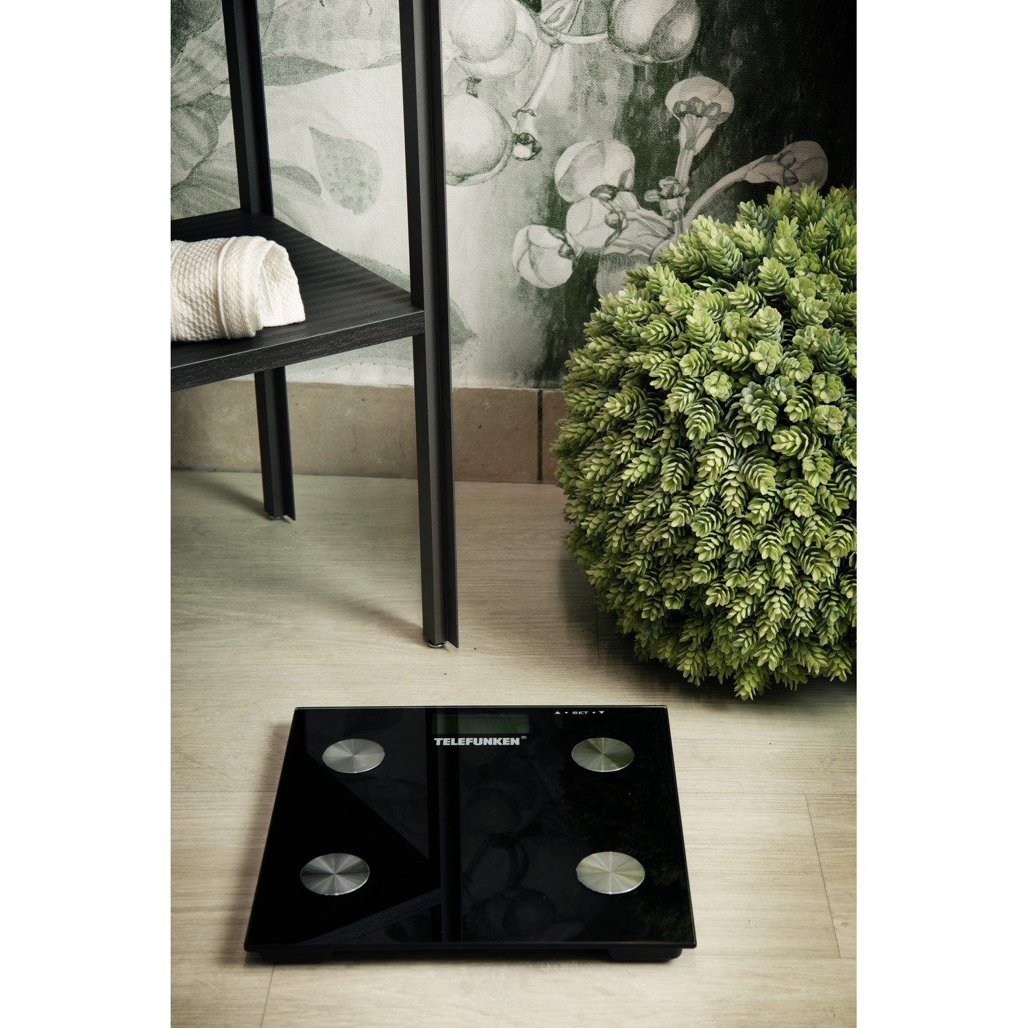 Una bilancia Telefunken nera su un pavimento in legno, con uno sfondo decorativo.