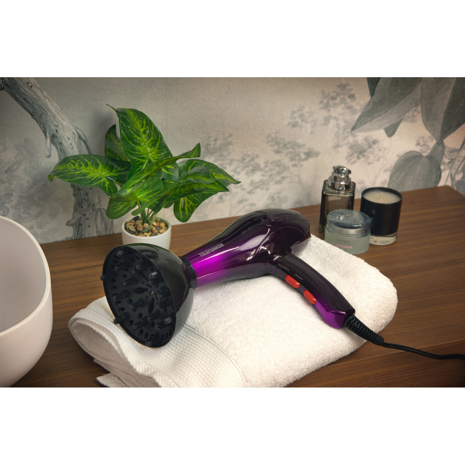 Asciugacapelli con sfumatura viola, su un asciugamano bianco, con piante e accessori.