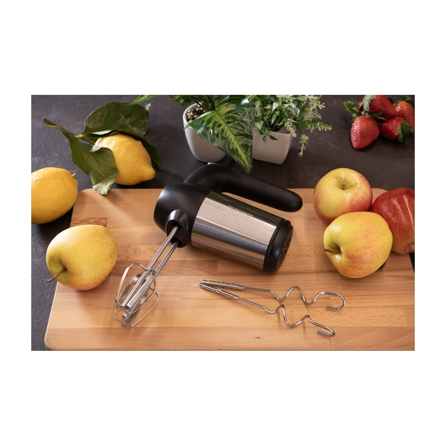 Un frullatore a mano nero e argento con accessori, mele e limoni su una superficie di legno.