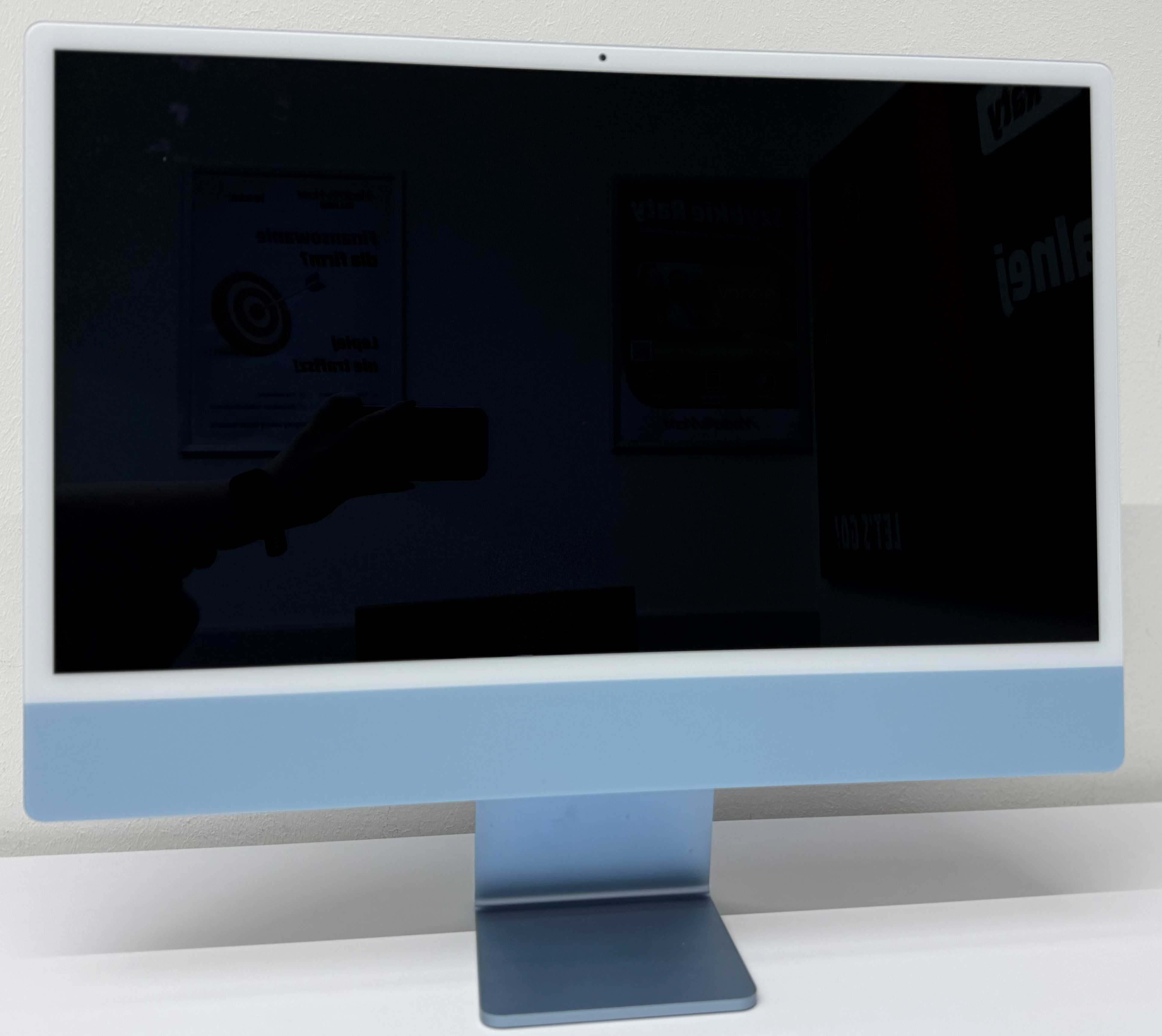 Monitor z niebieską ramką, odbijający ciemny pokój i białe biurko.