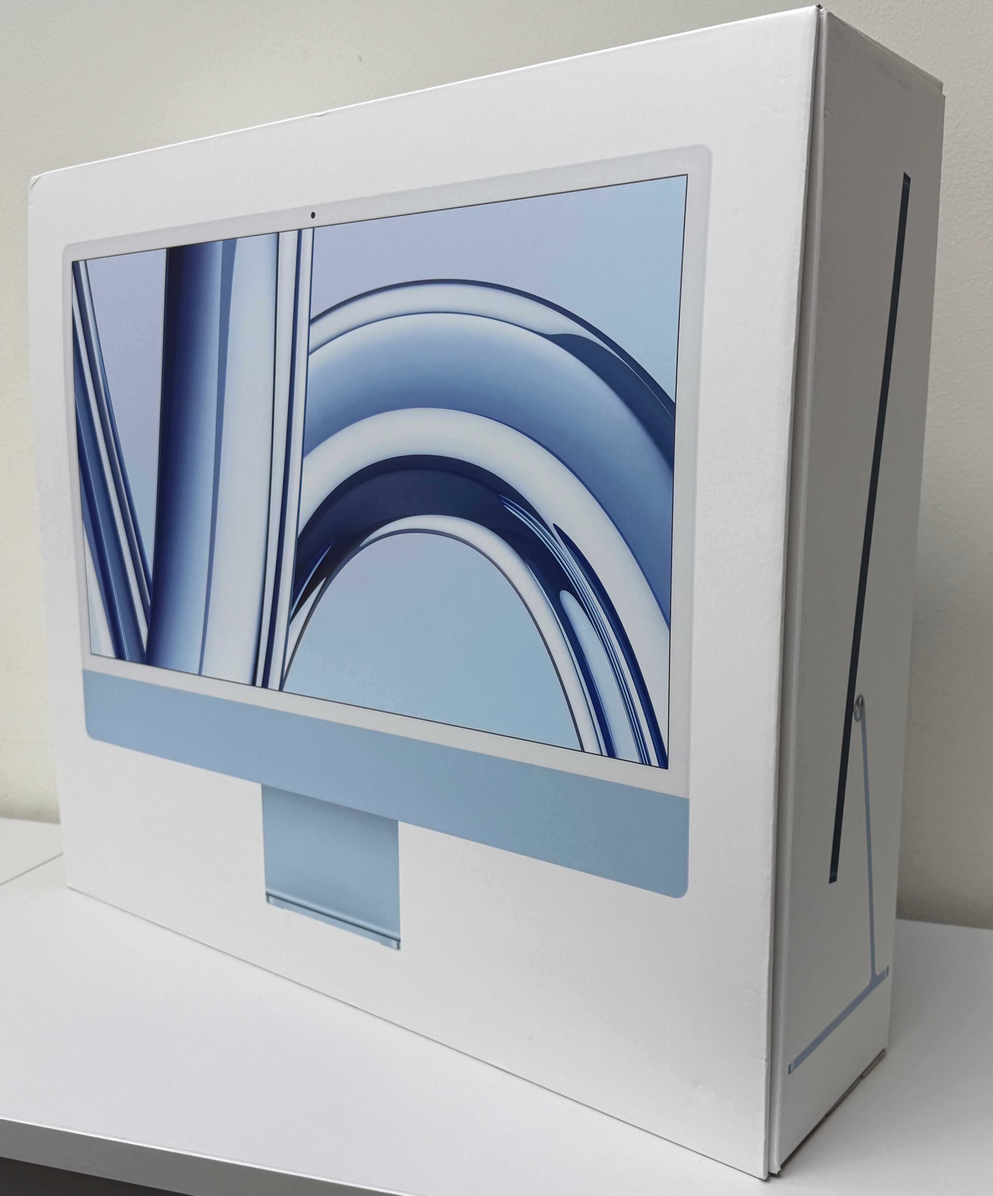 Niebieski iMac w białym pudełku stoi na białej powierzchni.