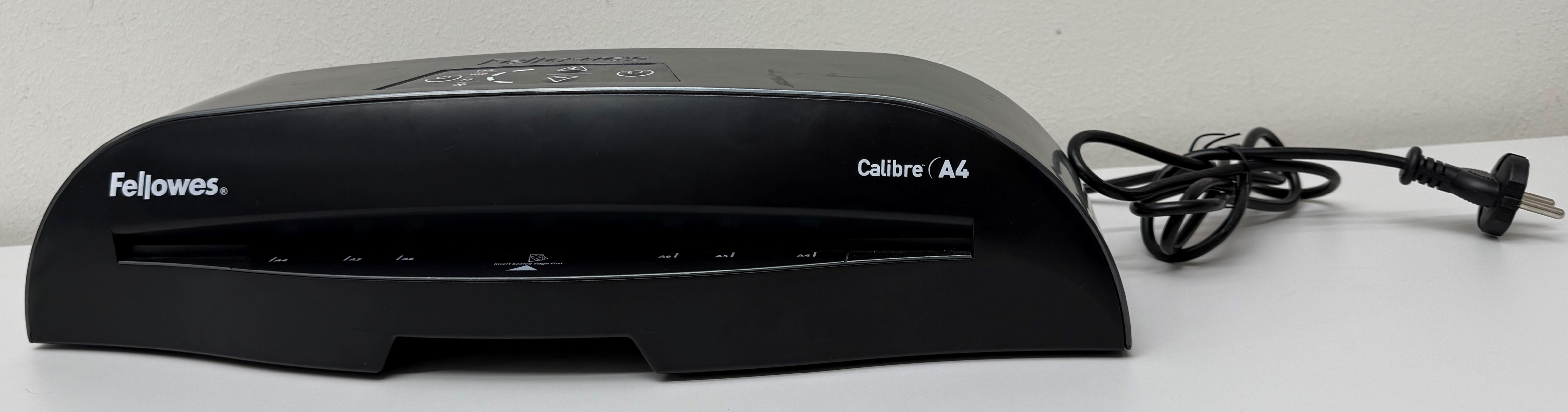 Czarna laminarka Fellowes Calibre A4 na białej powierzchni z kablem zasilającym. Produkt znajduje się na białej powierzchni.