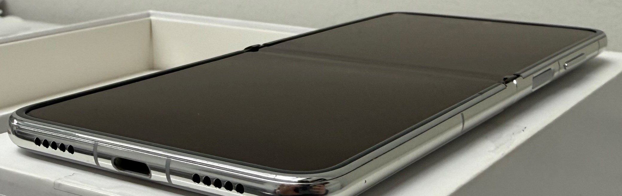 Czarny, składany smartfon, otwarty, na białej powierzchni, z białą skrzynką w tle.