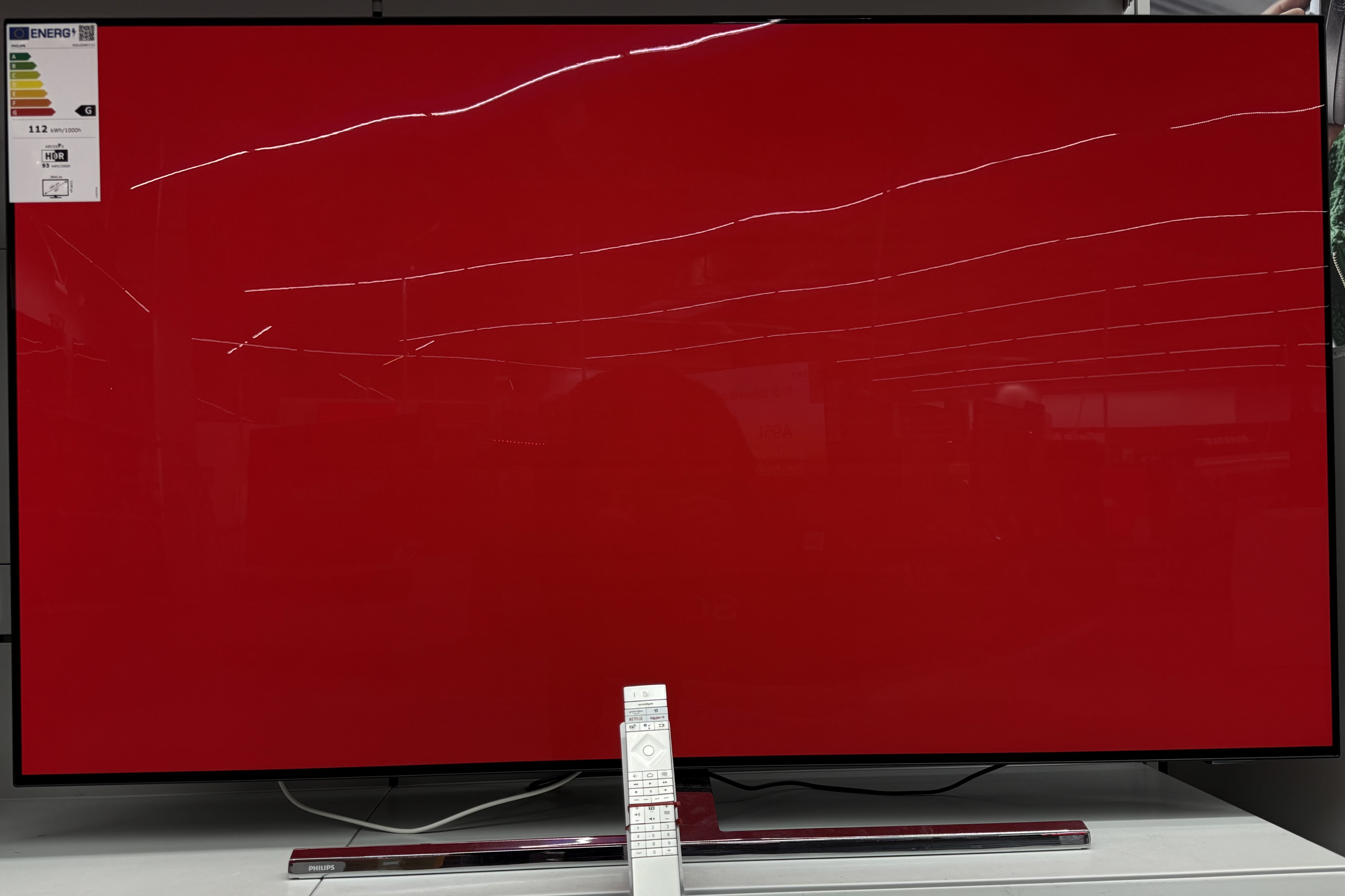 Duży czerwony ekran telewizora z pilotem z przodu. Ekran jest włączony.