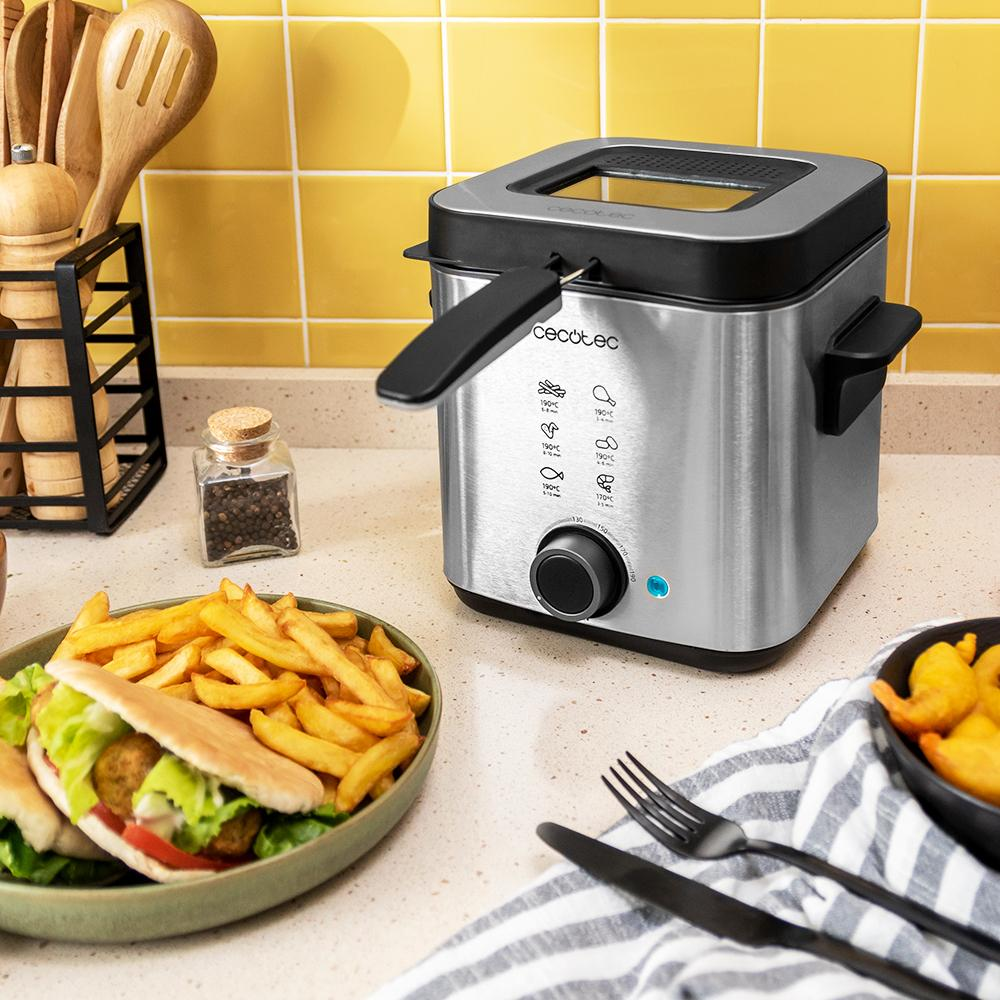Una freidora de acero inoxidable en una encimera de cocina, con comida y utensilios cerca.
