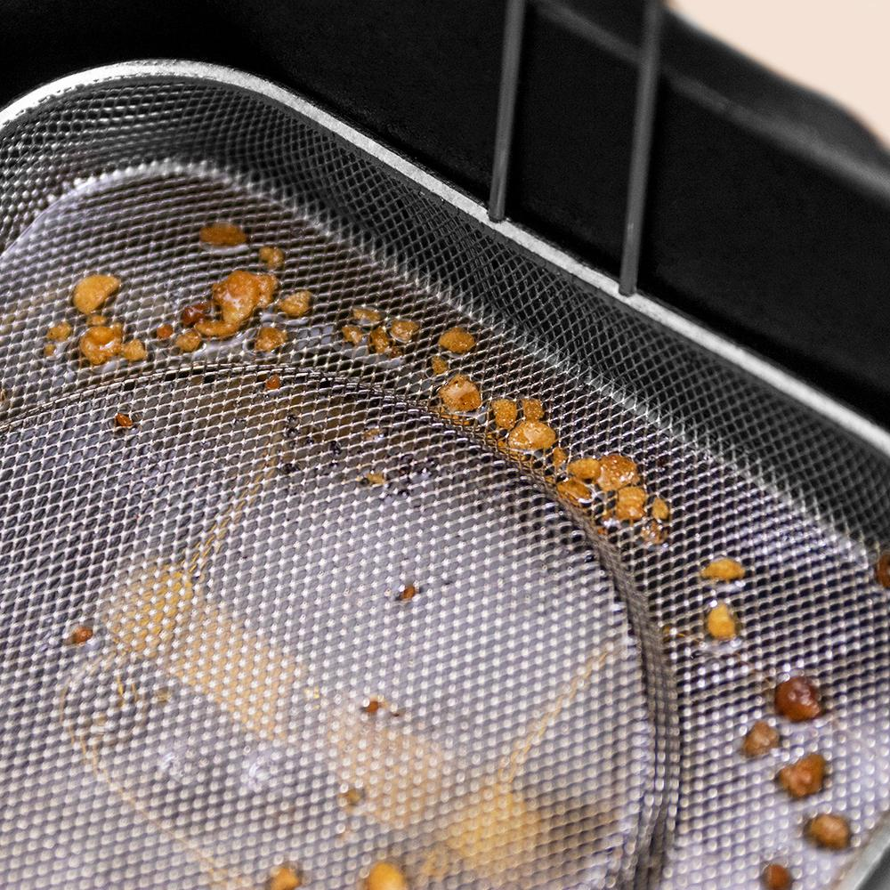 Primer plano de una cesta de freidora con residuos de alimentos fritos visibles en la malla.