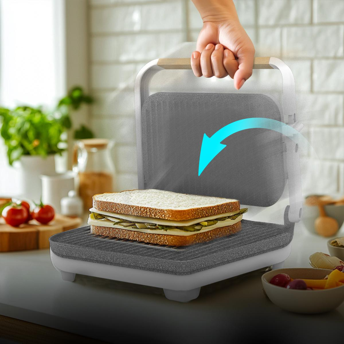 Un sándwich en una parrilla, con una mano cerrando la tapa. Otros ingredientes son visibles.