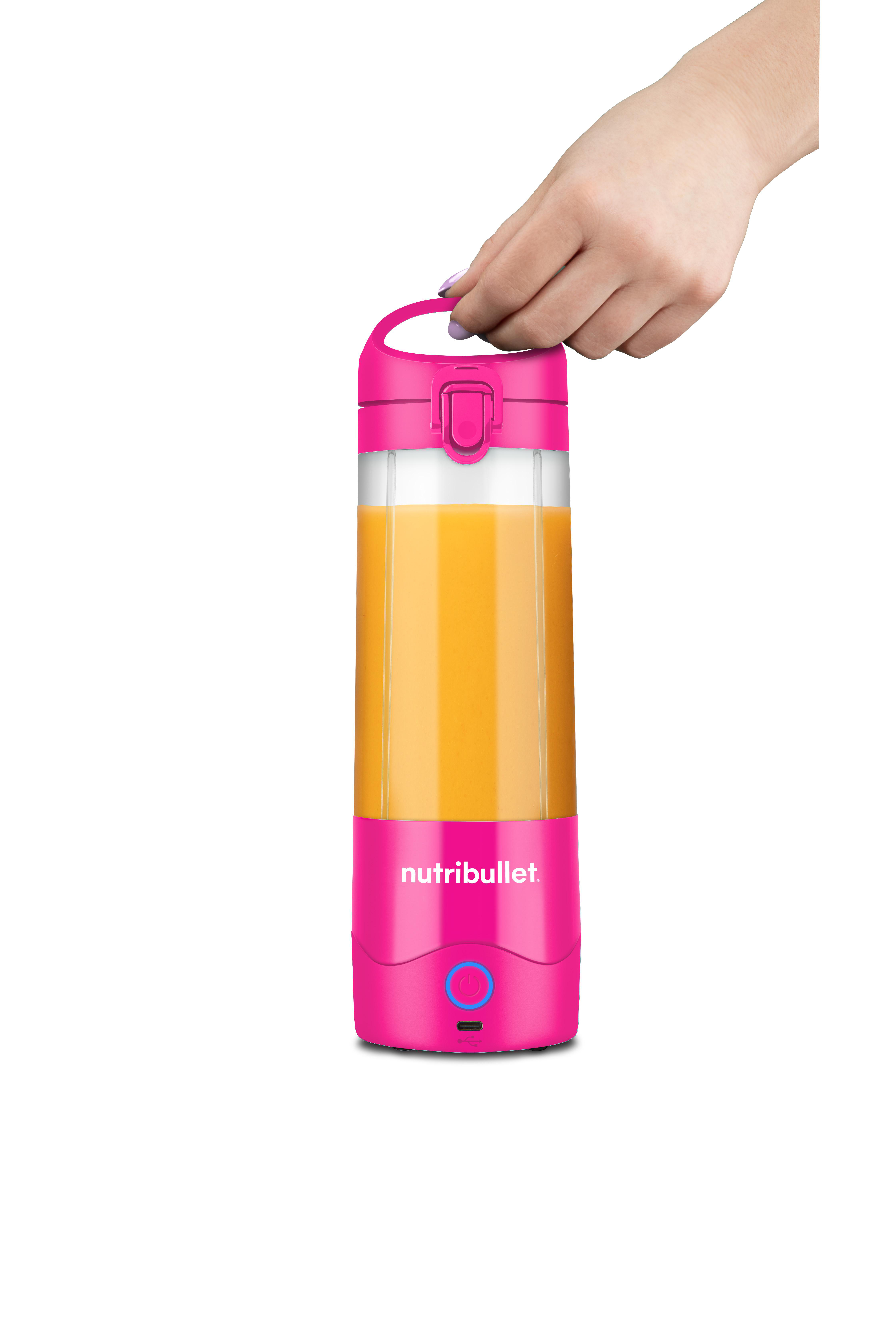 Eine Hand hält einen rosa Nutribullet-Mixer, gefüllt mit Orangensaft. Weißer Hintergrund.