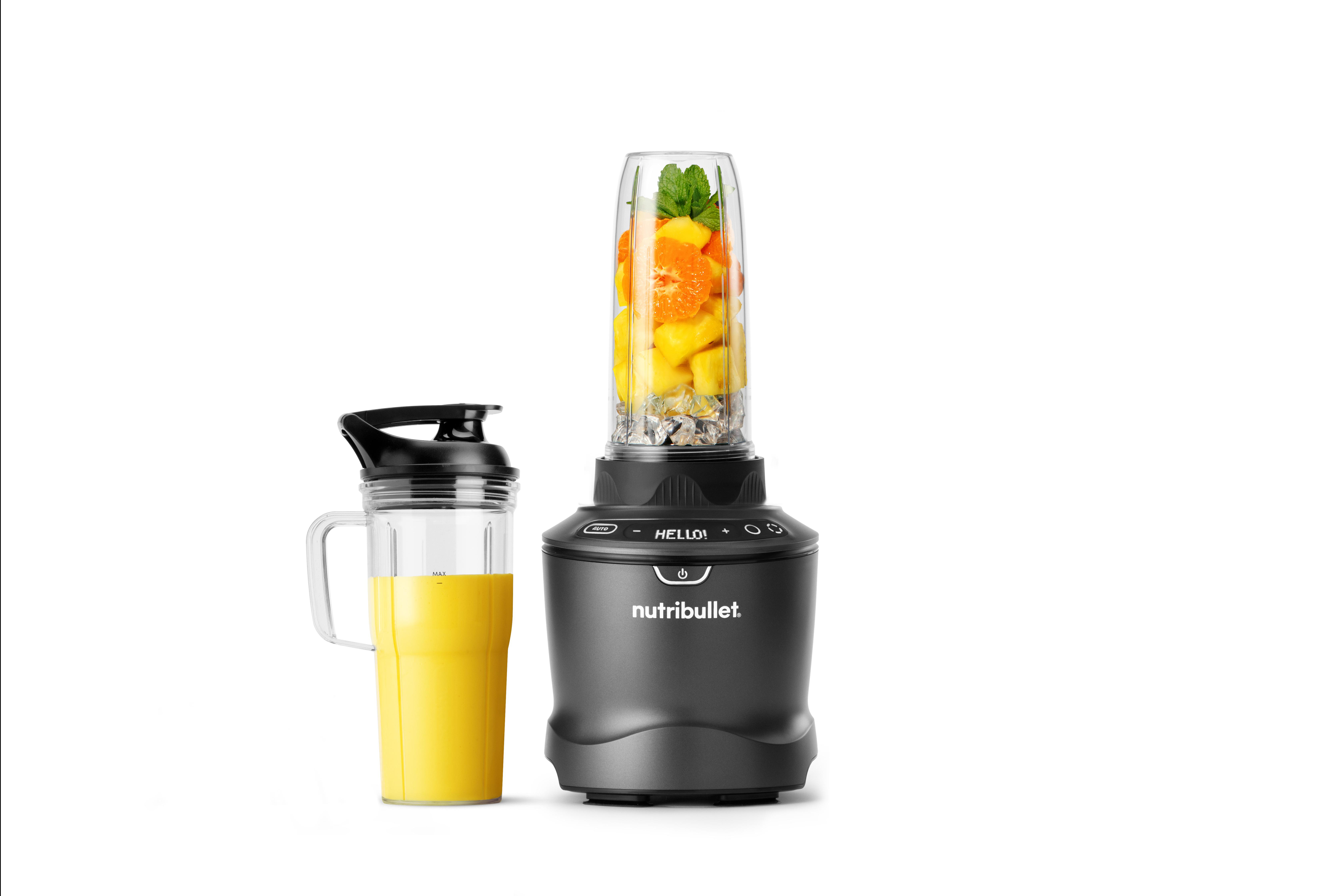 Ein Mixer mit einem Becher gelber Flüssigkeit und einem Behälter mit Früchten. Es ist auf weißem Hintergrund.
