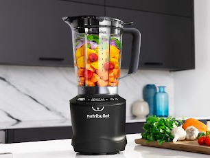 Schwarzer Mixer mit Zutaten im Inneren. Er steht auf einer weißen Arbeitsplatte.