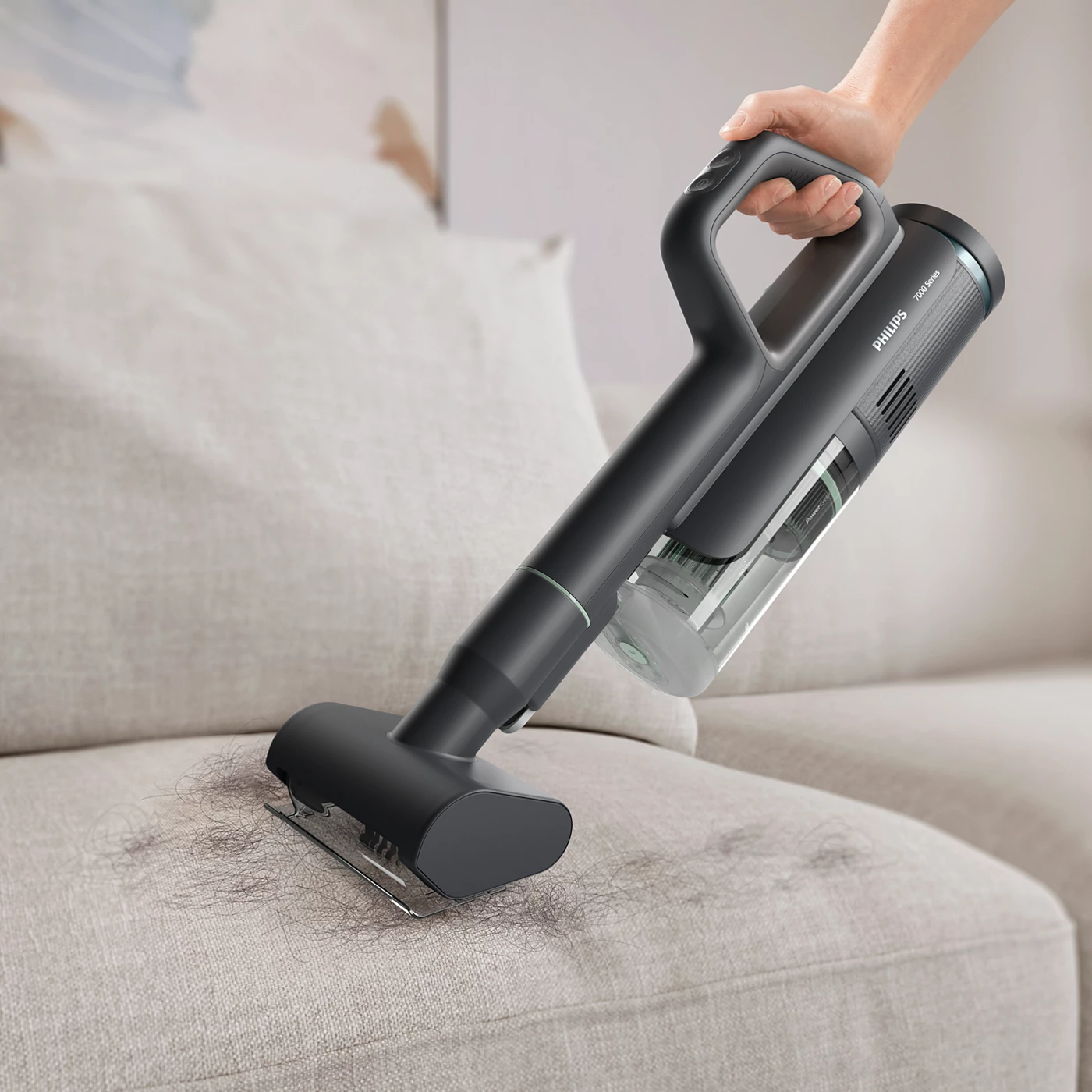 Une personne utilise un aspirateur Philips sans fil pour nettoyer un canapé, en enlevant les cheveux et les débris.