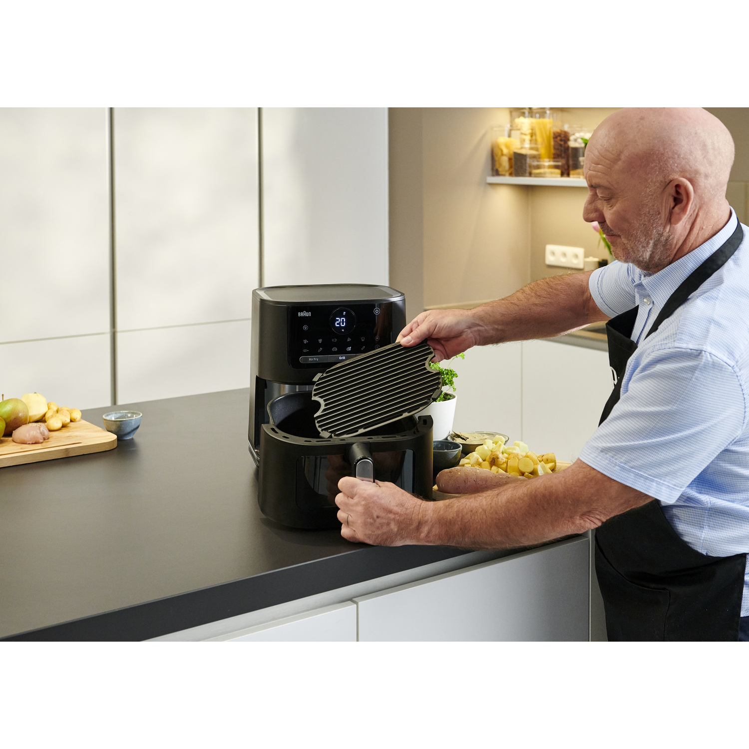 Un homme met une grille dans une friteuse à air noire sur un comptoir de cuisine.