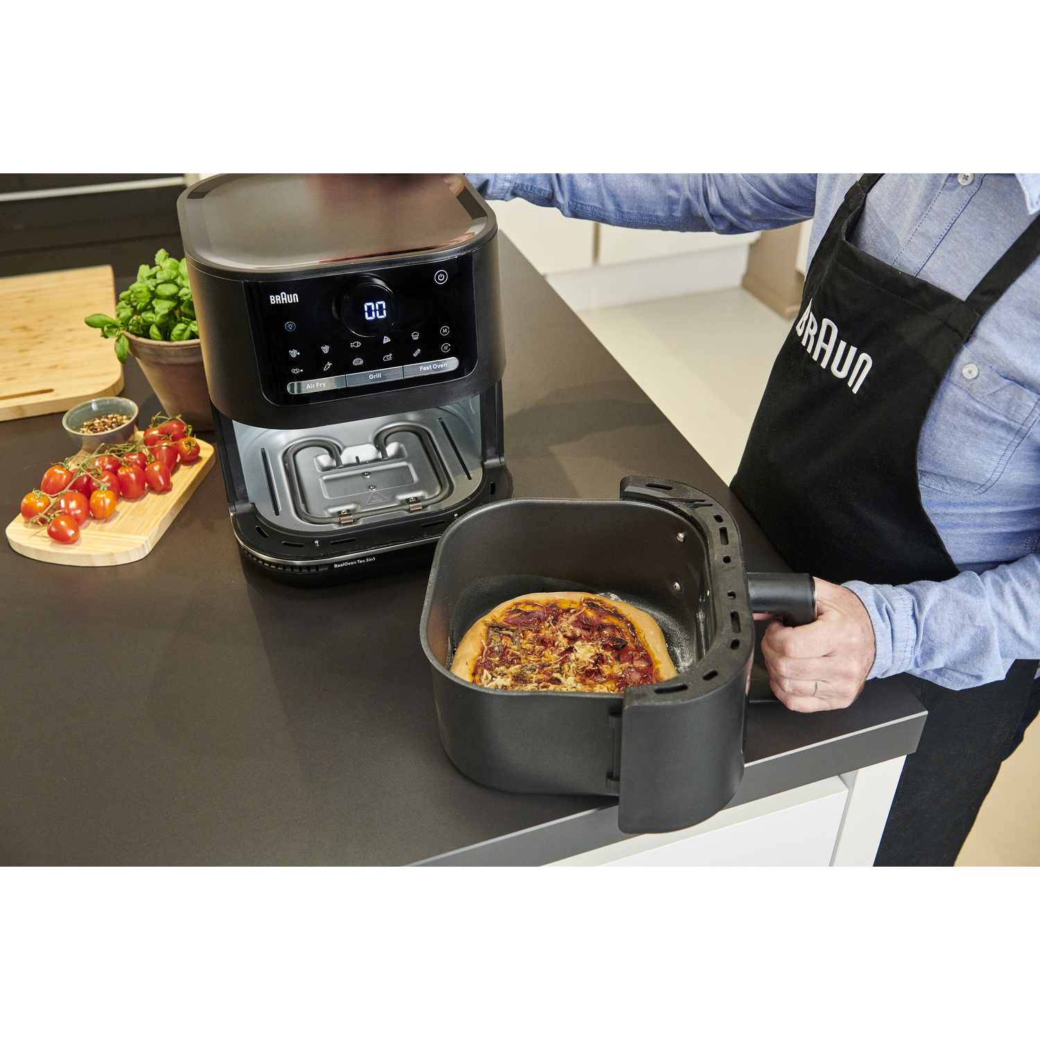 Personne retirant une pizza d'une friteuse à air noire. Comptoir avec pizza et ingrédients.