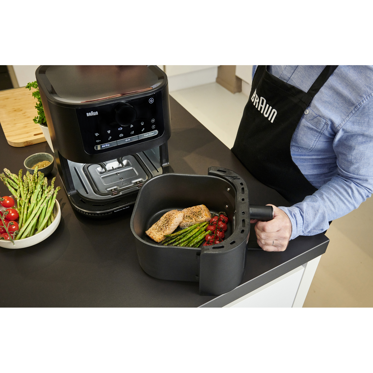 Personne cuisinant avec une friteuse à air noire, légumes et poisson.
