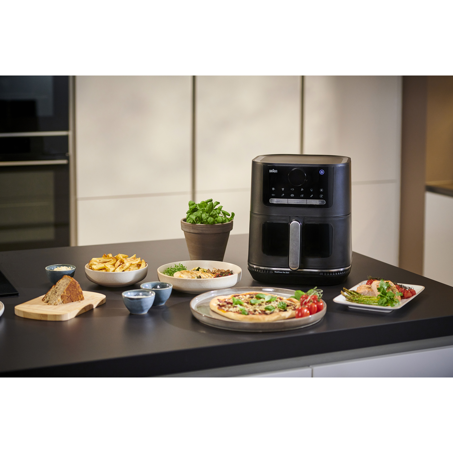Friteuse à air avec nourriture, pizza, frites et petites plantes sur un comptoir de cuisine.