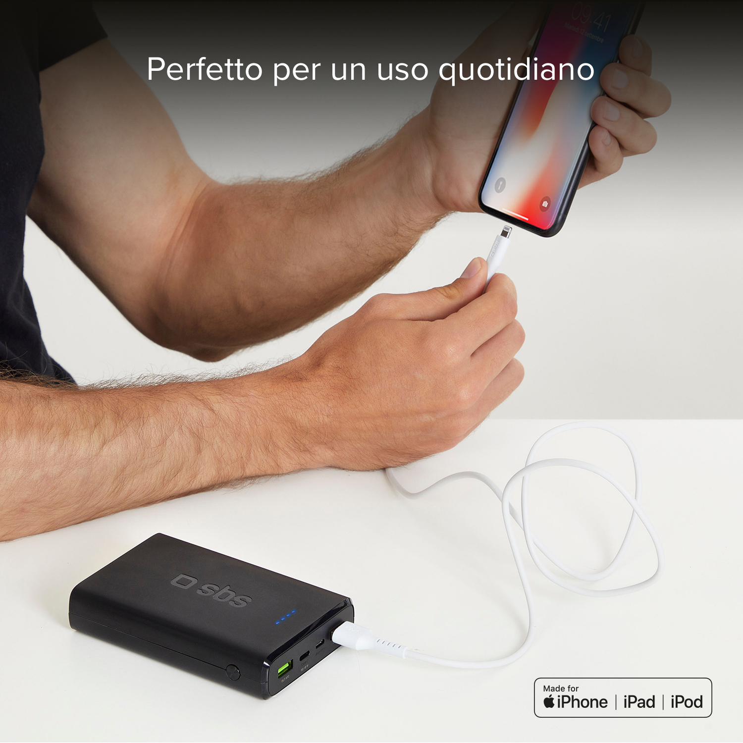 A person charges a phone with a black power bank. The phone is white. The table is white.
