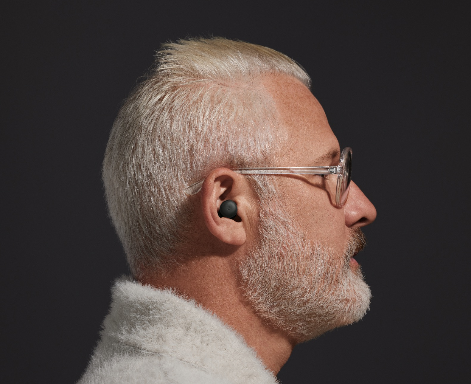 Profil eines Mannes mit grauem Haar und Bart, Brille und Ohrhörern im Ohr.