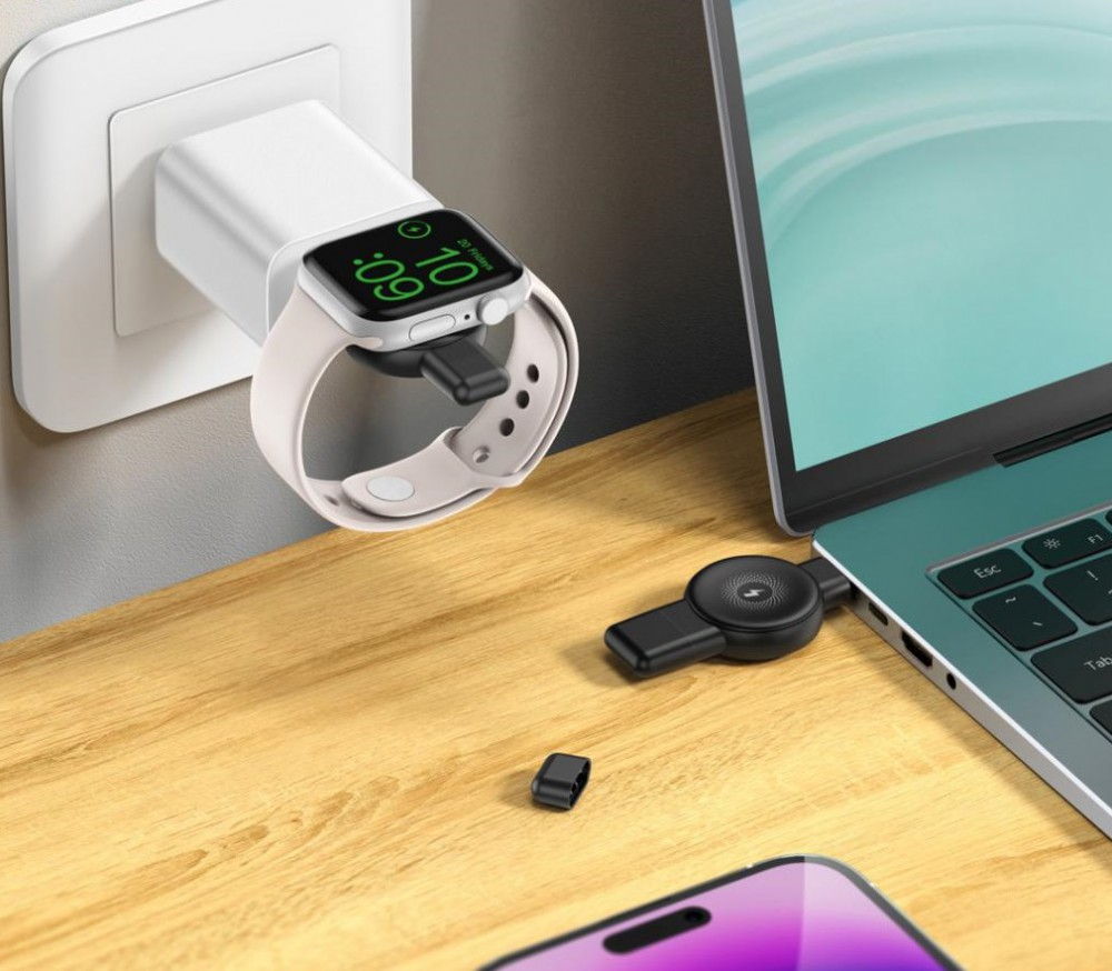 Egy fehér Apple Watch töltődik fali aljzatról. Laptop a közelben. Fekete töltőkábel és egy kis darab.