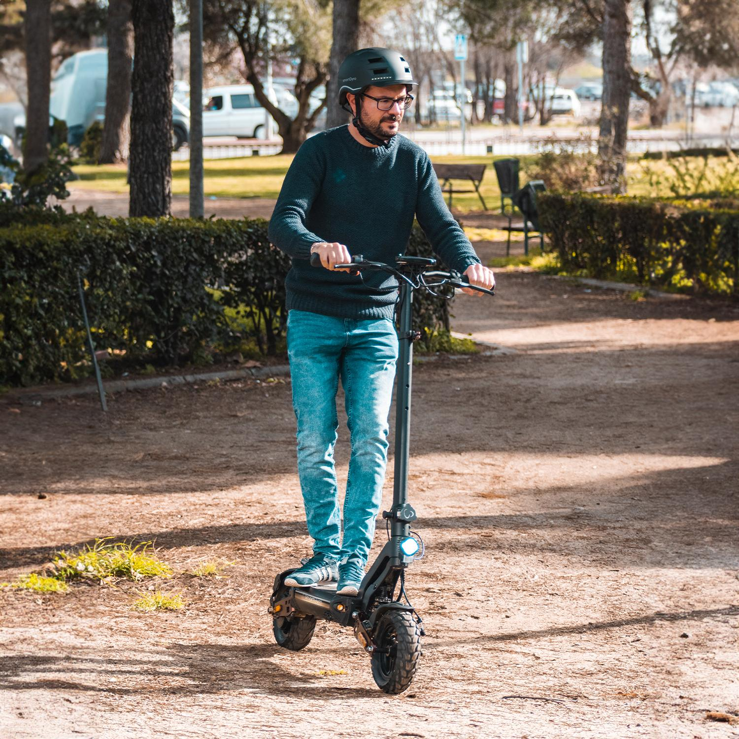 Un hombre montando un patinete eléctrico en un parque.