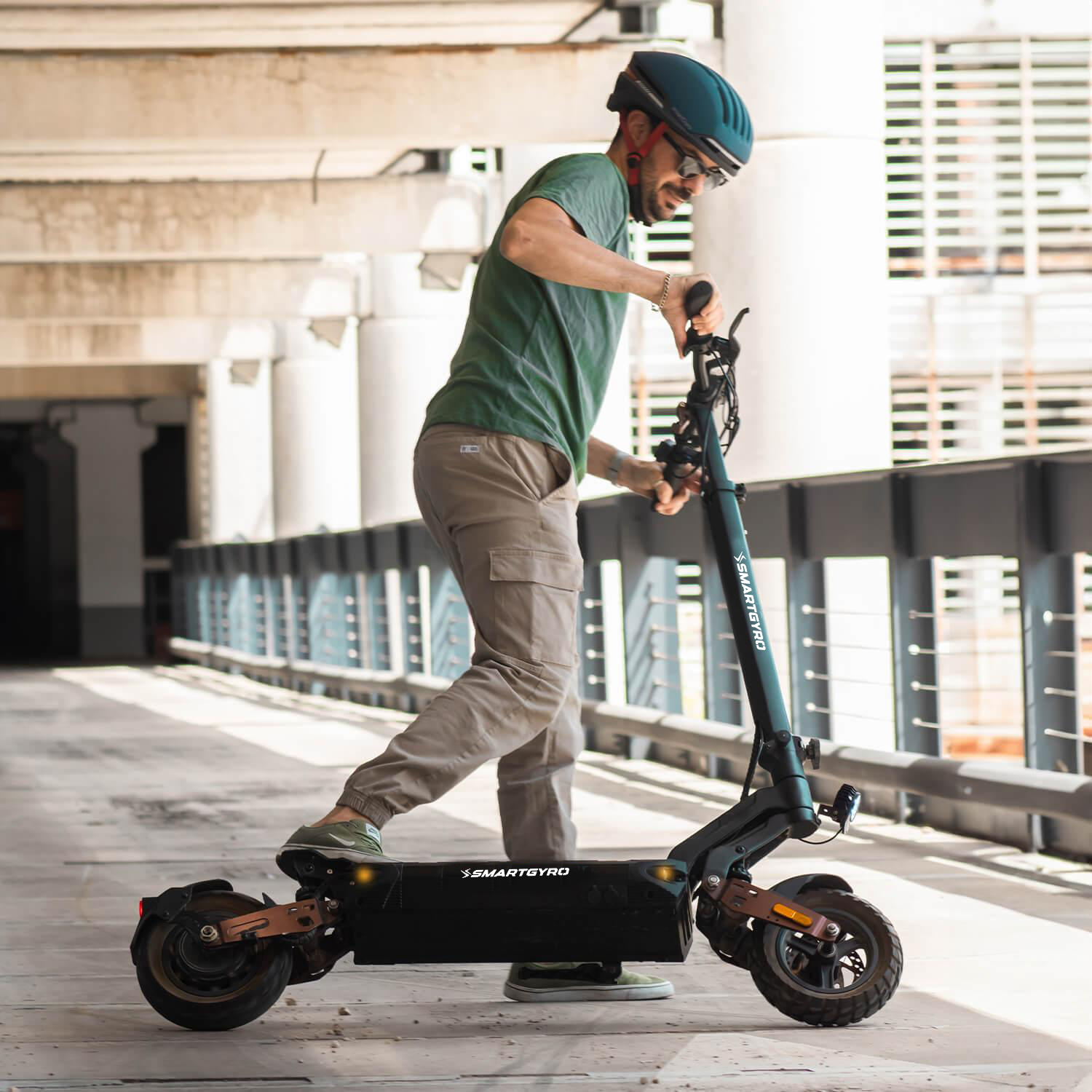 Un hombre con camisa verde y casco montando un scooter negro sobre suelo de hormigón.