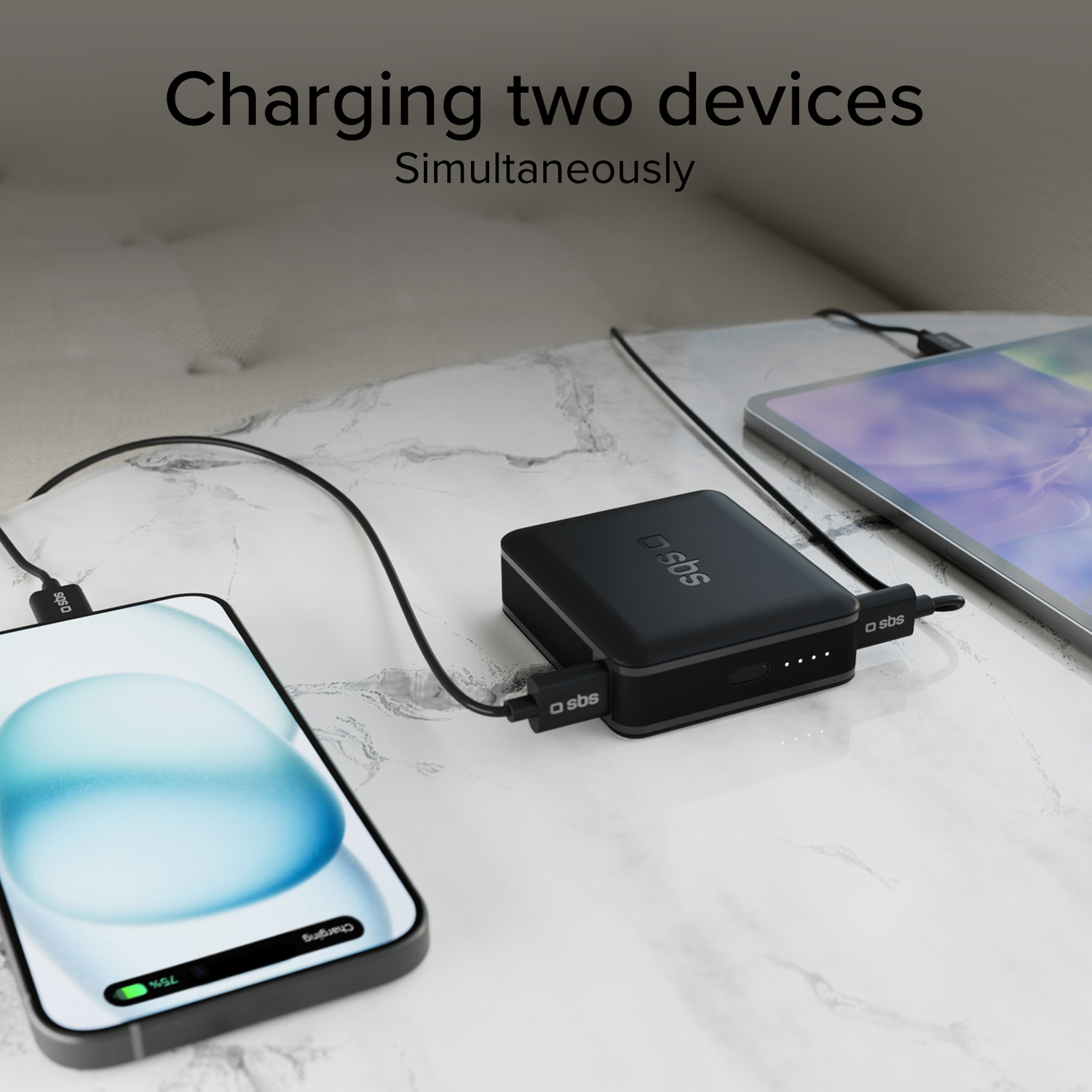 Black power bank charging phone and tablet. Cables connect devices. Table top in the background.