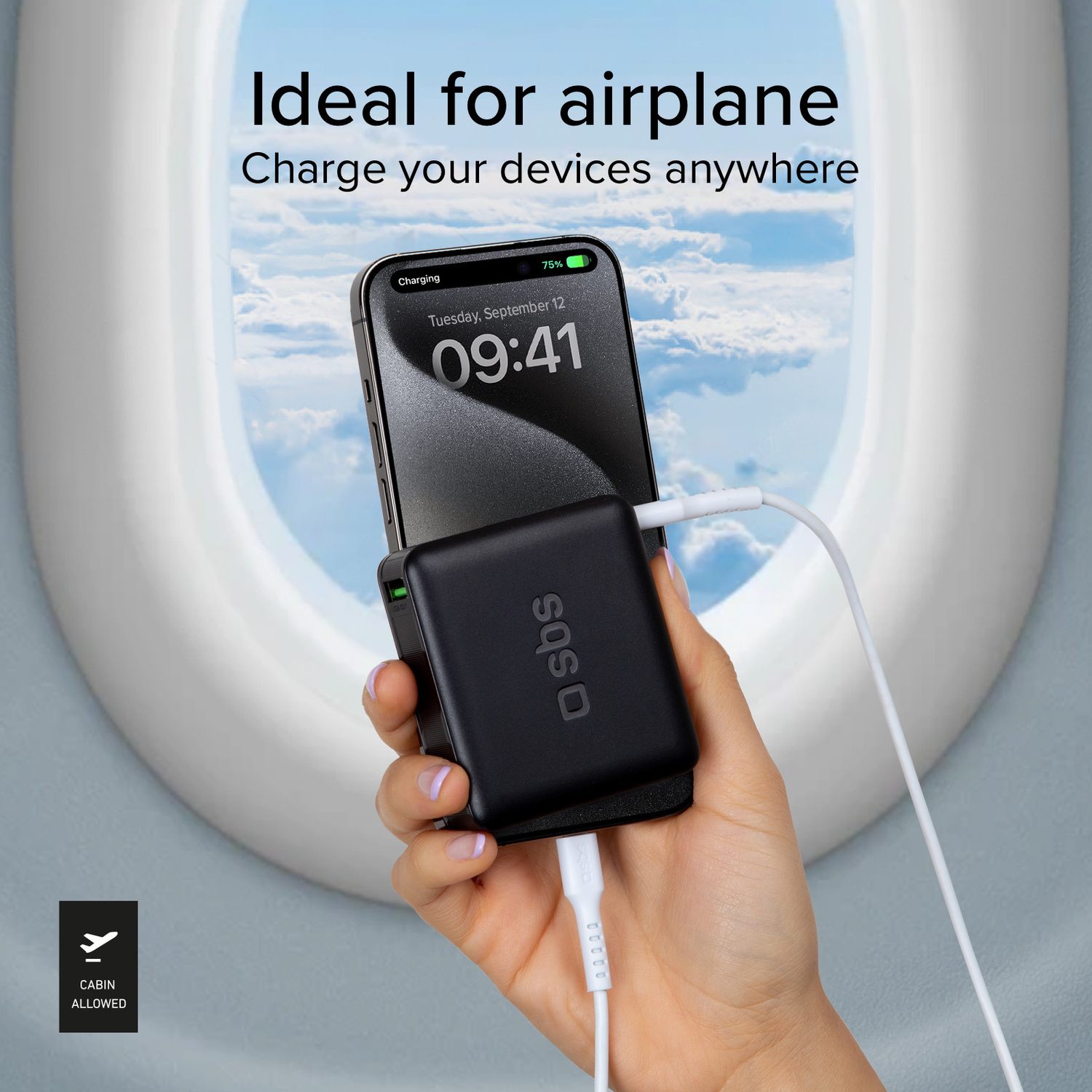 A hand holding a black charger and a phone charging on an airplane, with a window view.