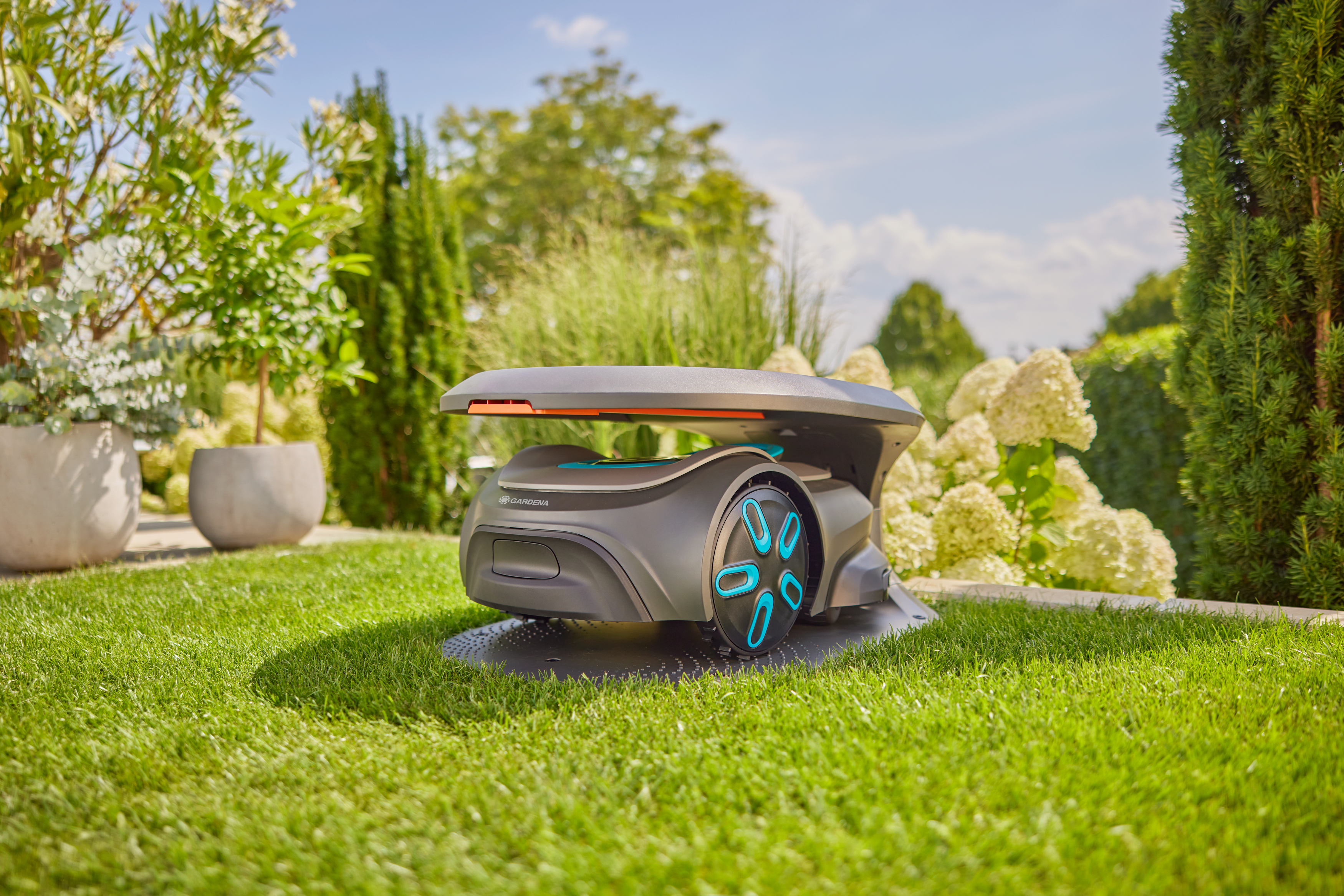 Robotischer Rasenmäher auf Gras, umgeben von Pflanzen und Bäumen, unter hellem Himmel.