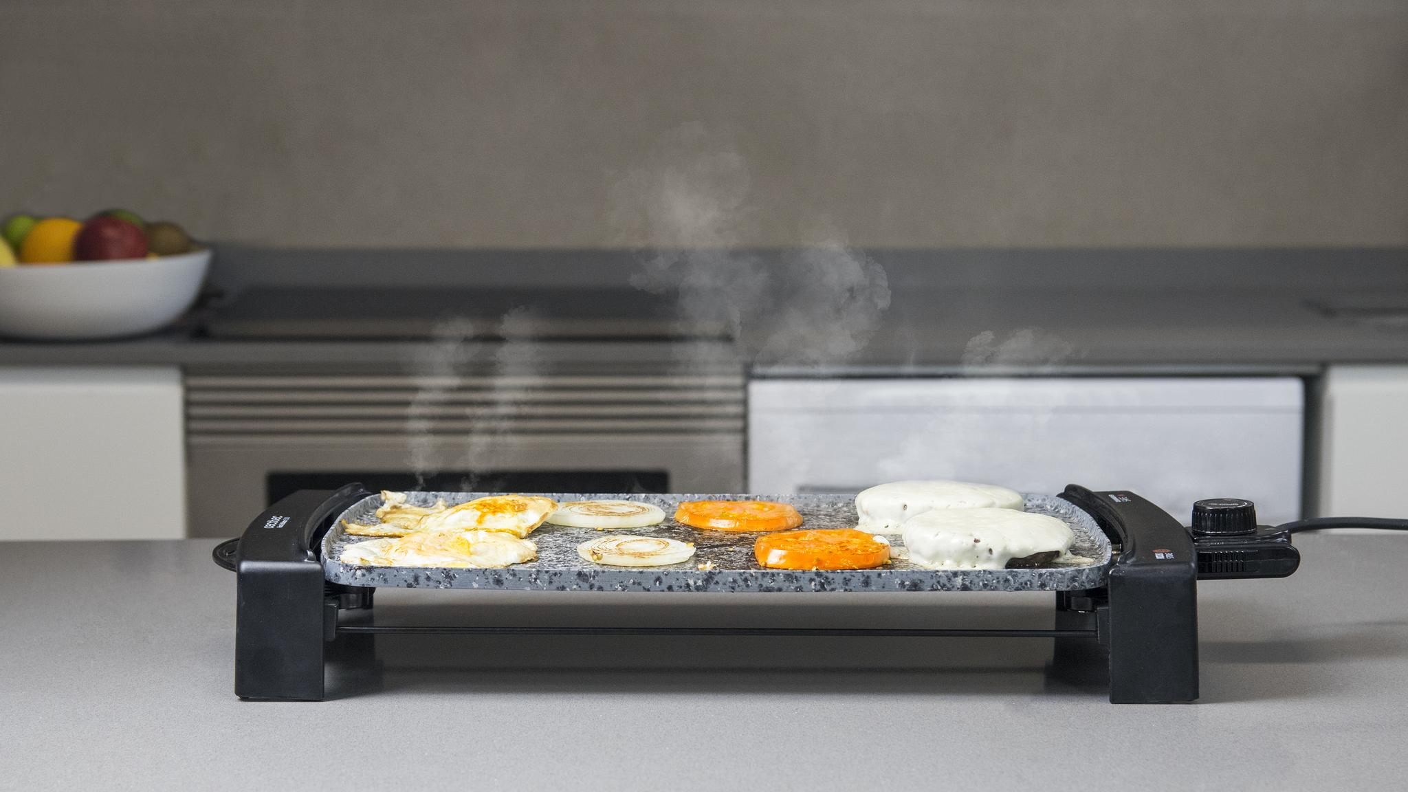 Parrilla con comida sobre una encimera. Vapor ascendente. Combinación de colores gris y blanco.