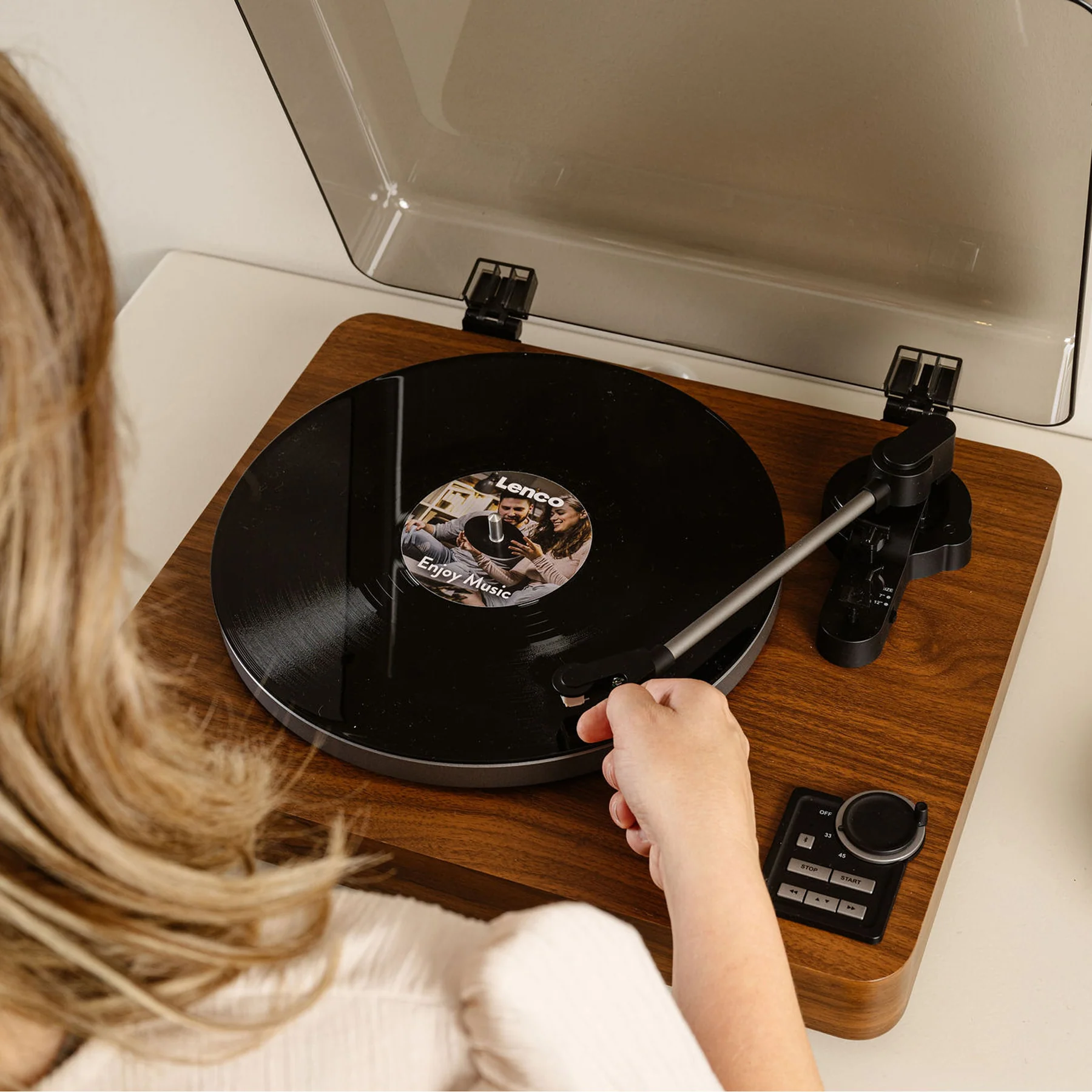 La main d'une personne plaçant l'aiguille sur un disque vinyle sur une platine en bois, avec vue sur l'étiquette.