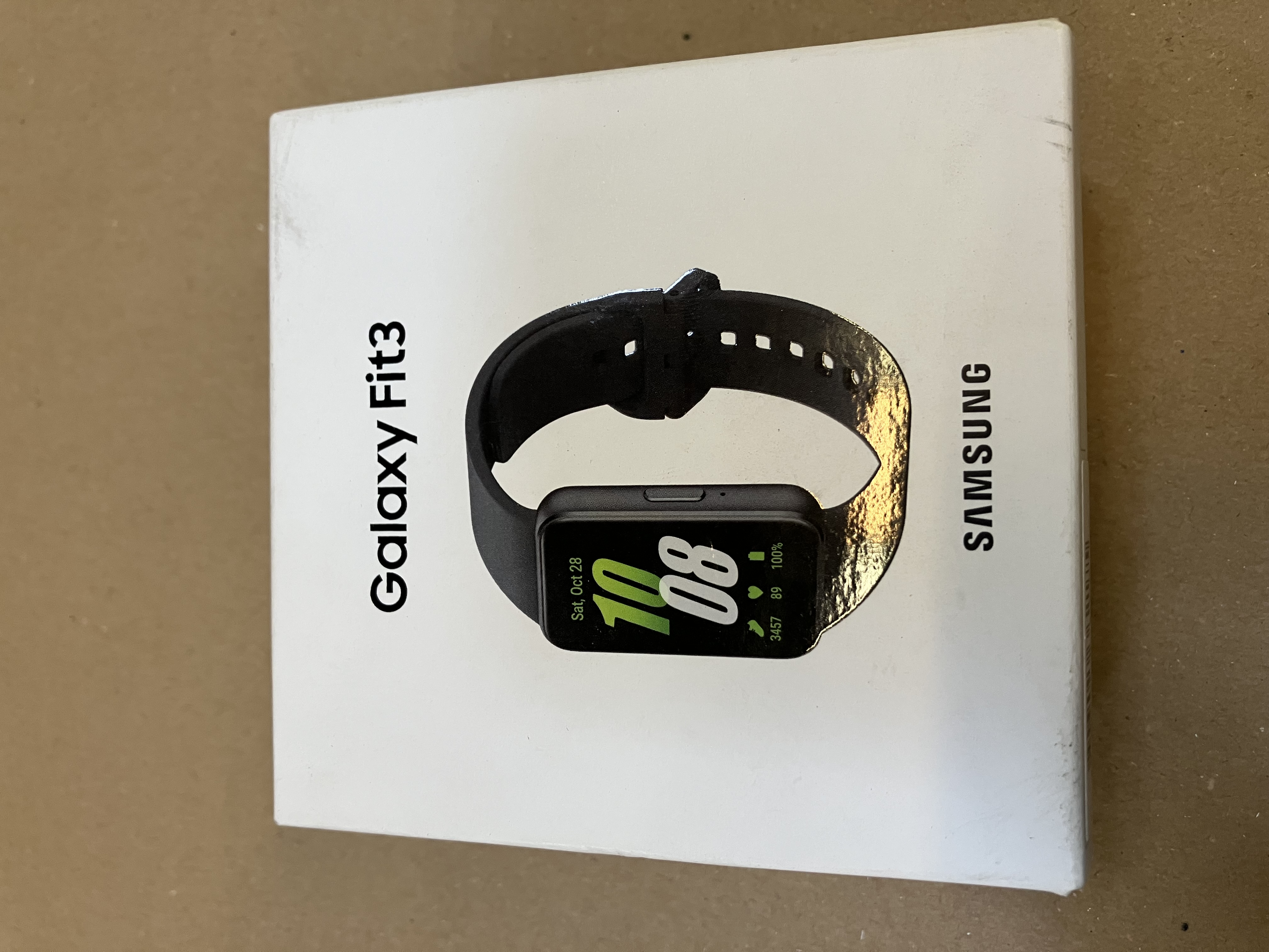 Pudełko z zegarkiem Samsung Galaxy Fit3. Zegarek jest czarny z zielonym wyświetlaczem i czarnym paskiem.