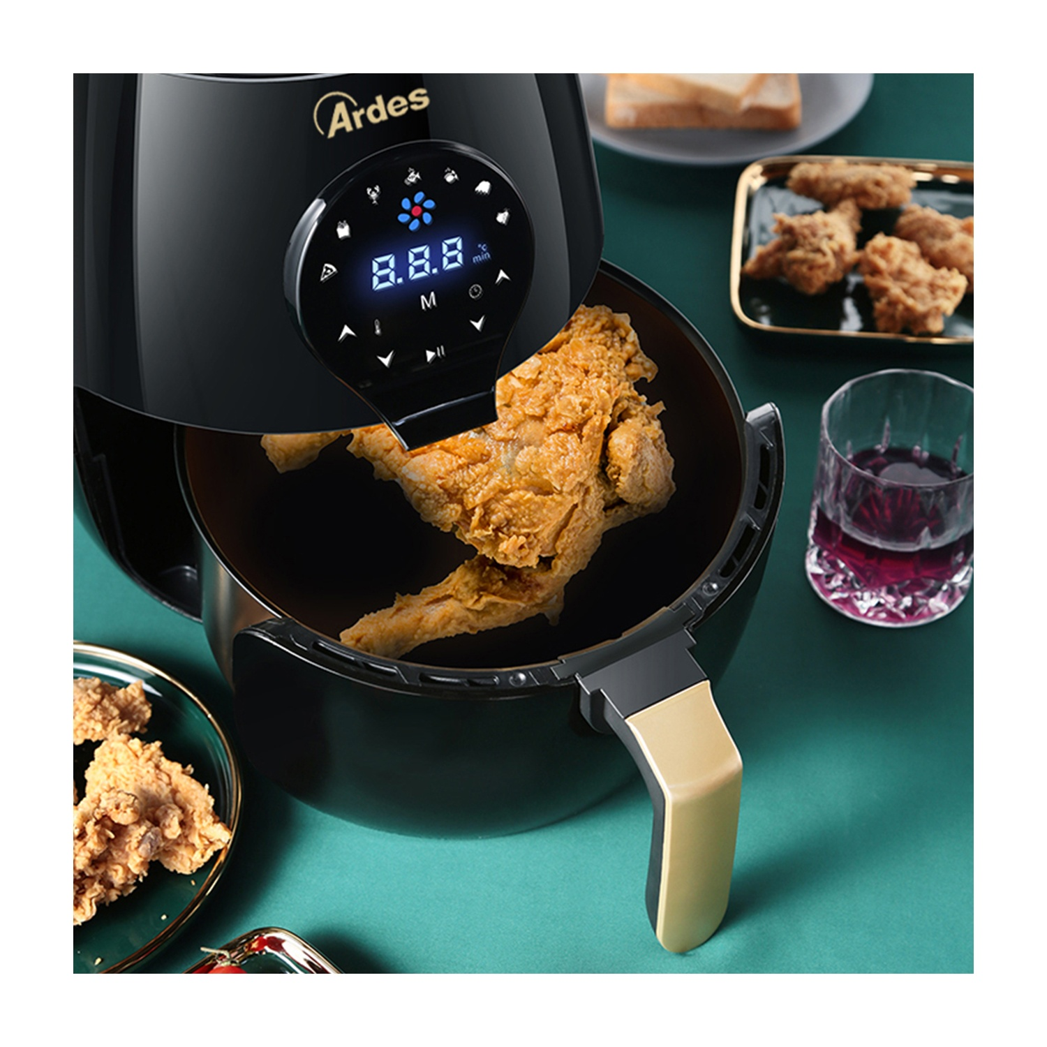 Friggitrice ad aria nera con pollo fritto dentro, bicchiere di vino e piatto di cibo fritto.