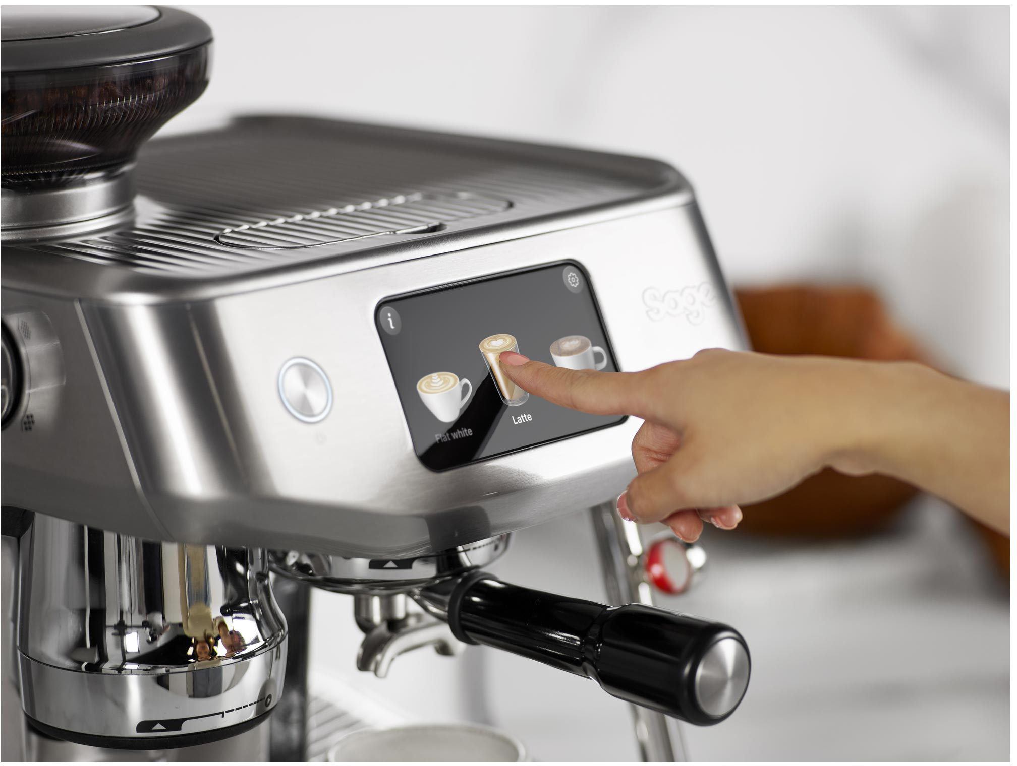 Egy személy keze a latte opcióra mutat egy ezüst eszpresszó gép érintőképernyőjén.