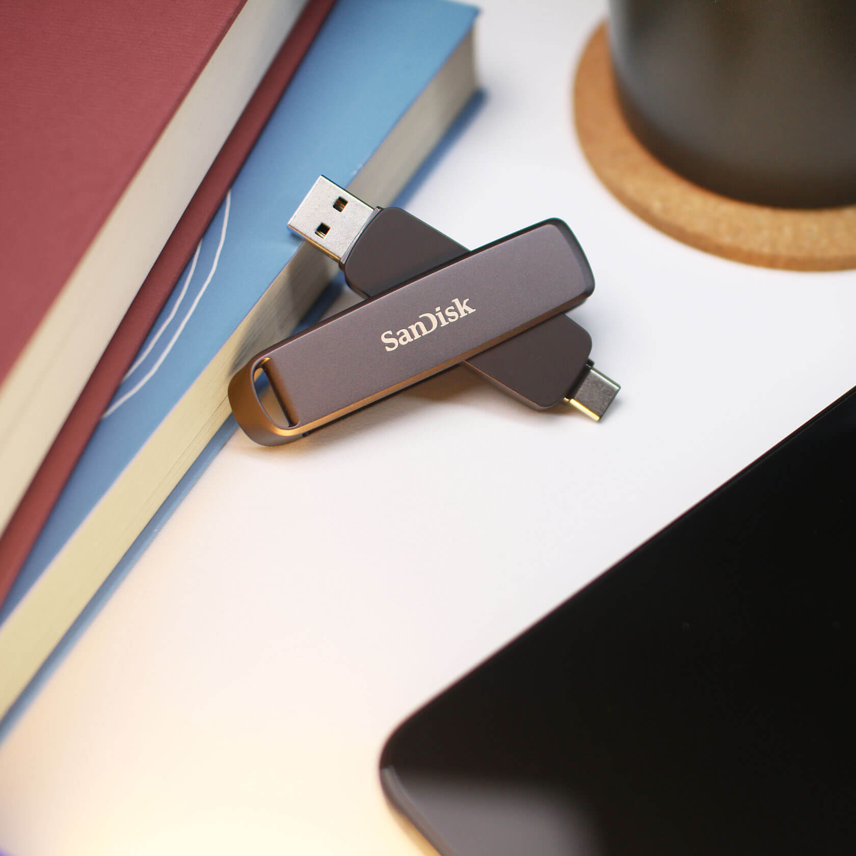 Zwei SanDisk USB-Laufwerke liegen auf einer weißen Oberfläche mit Büchern, einem Telefon und einem Untersetzer.