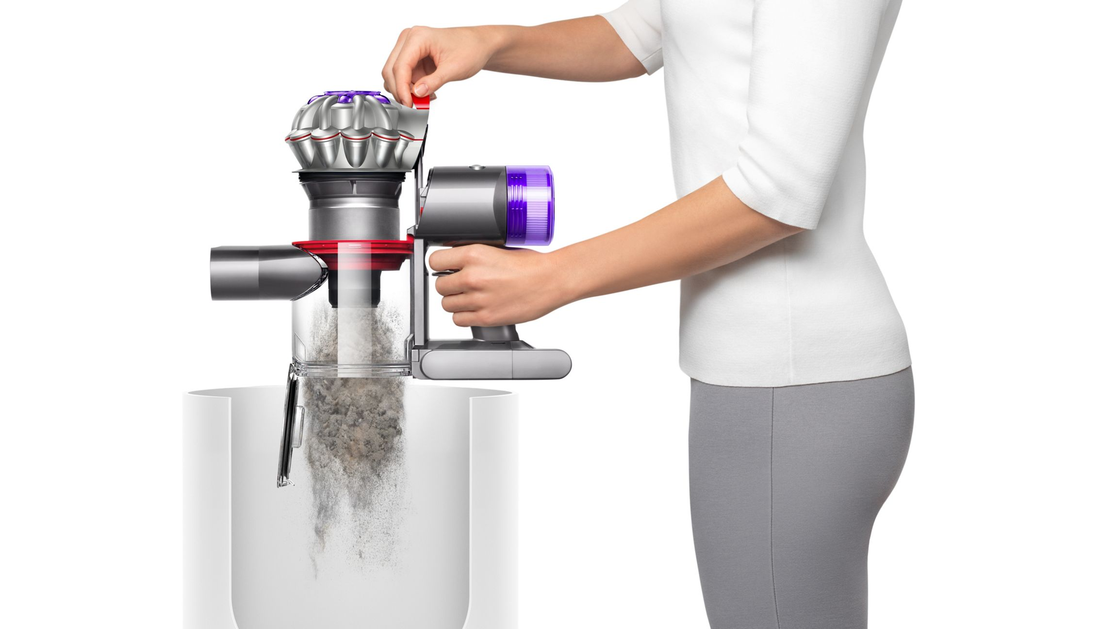 Bir kadın, Dyson elektrikli süpürgesini beyaz bir kutuya boşaltıyor, toz ve kalıntıları gösteriyor.