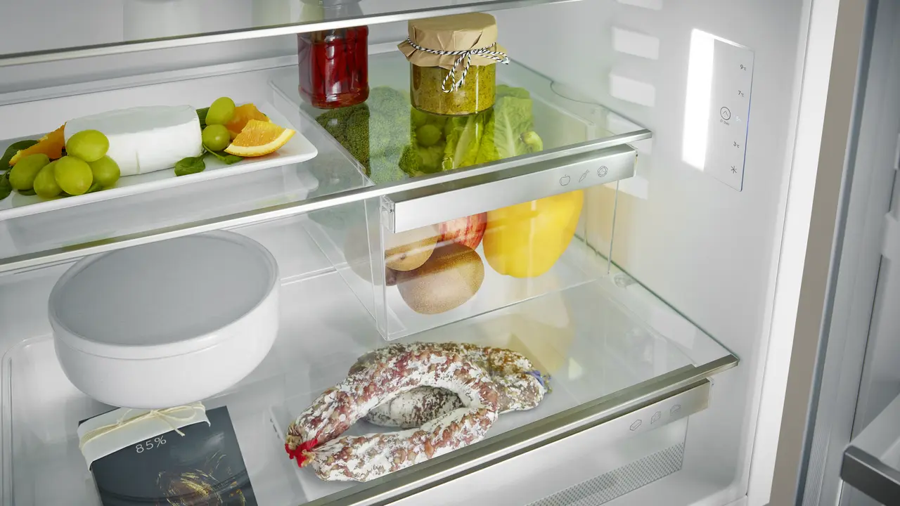 Kühlschrankinneres mit verschiedenen Lebensmitteln: Käse, Früchte, Gläser und Wurst.