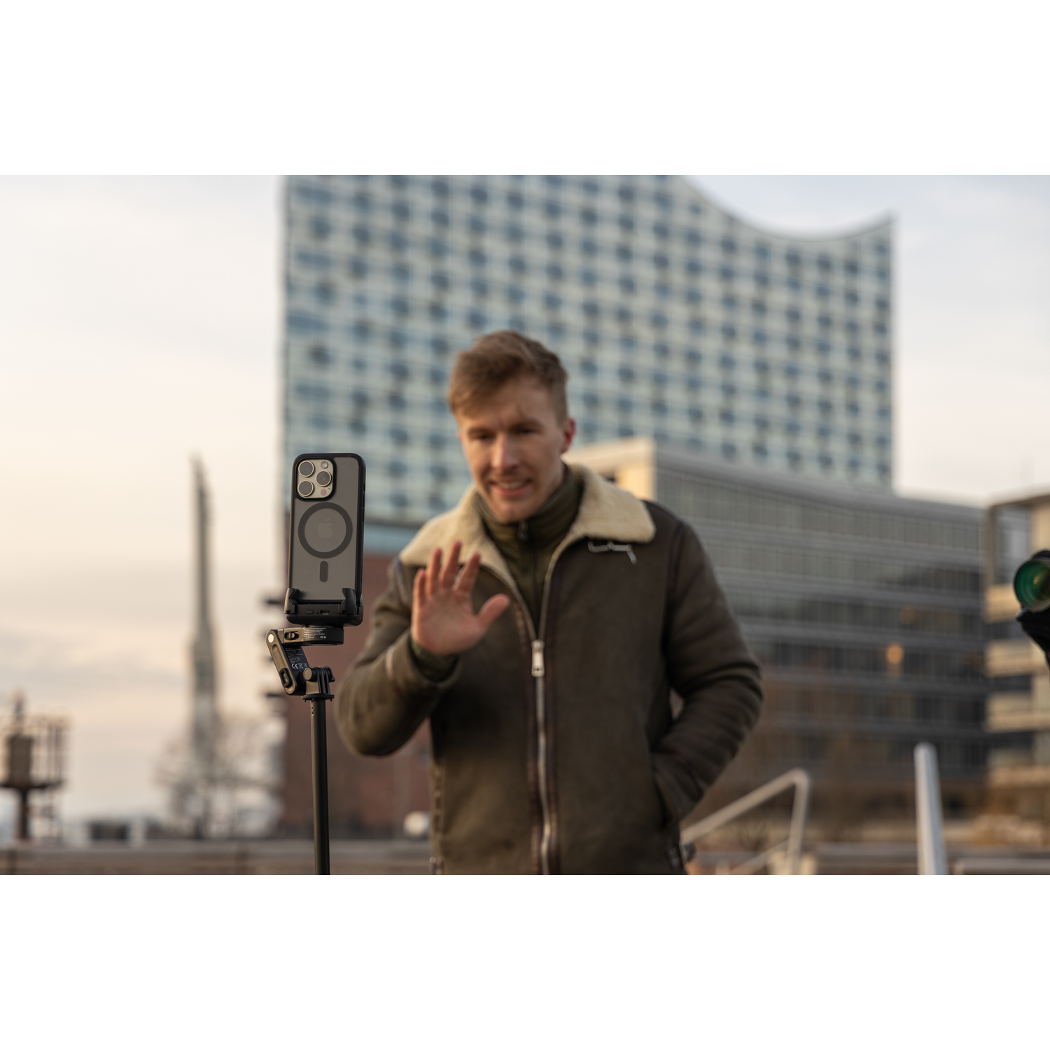 Man met telefoon op een statief, zwaaiend voor een gebouw.