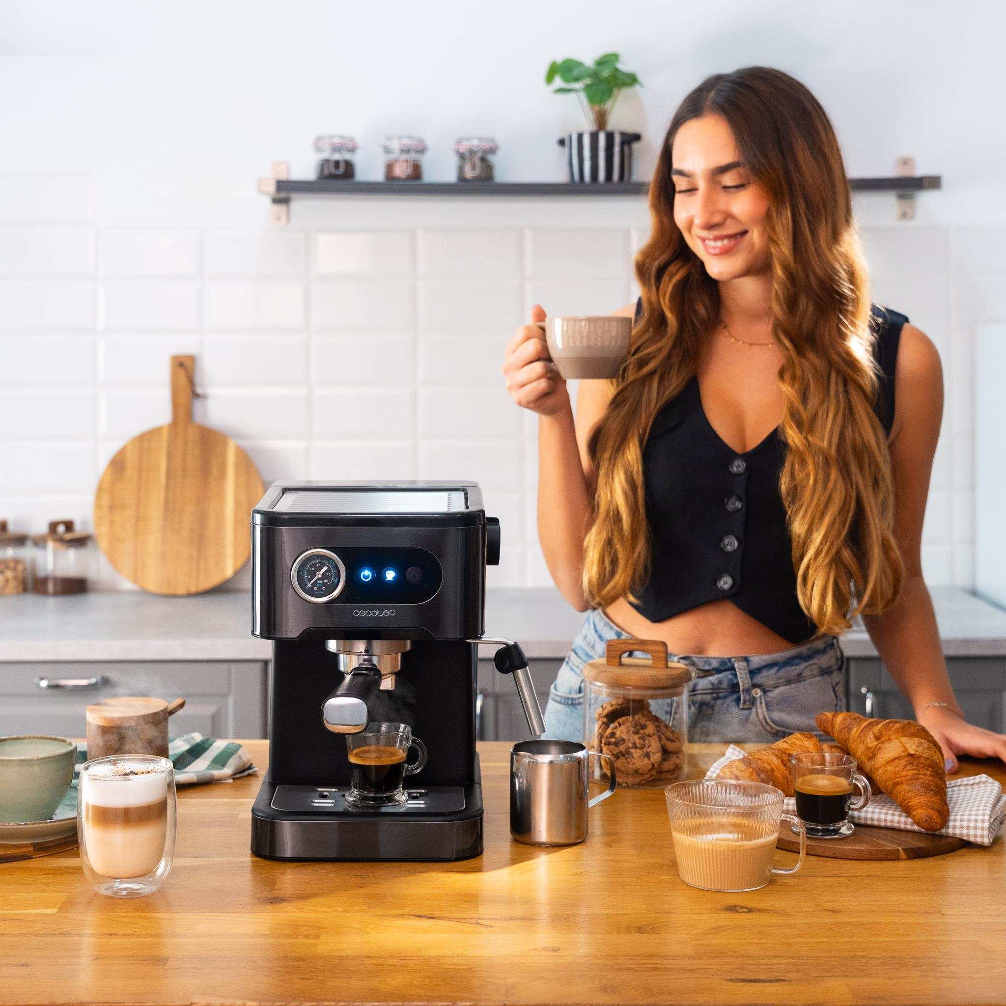 Una mujer en una cocina sosteniendo una taza de café, con una cafetera y comida en la mesa.