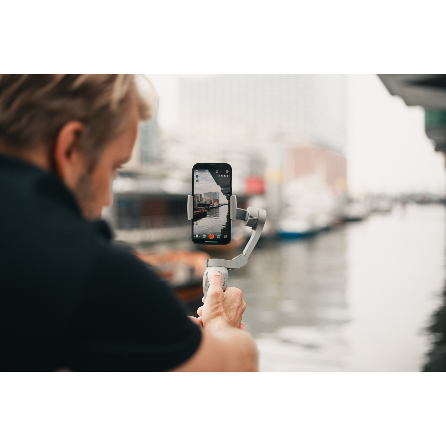 A man using a smartphone with a gimbal near a body of water.