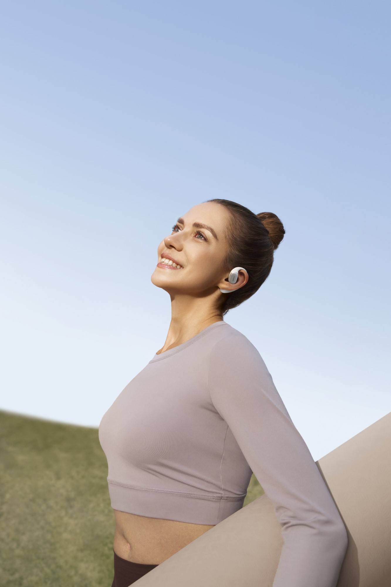 Kobieta patrzy w górę w niebo, nosząc słuchawki i jasną koszulę. Trzyma coś.