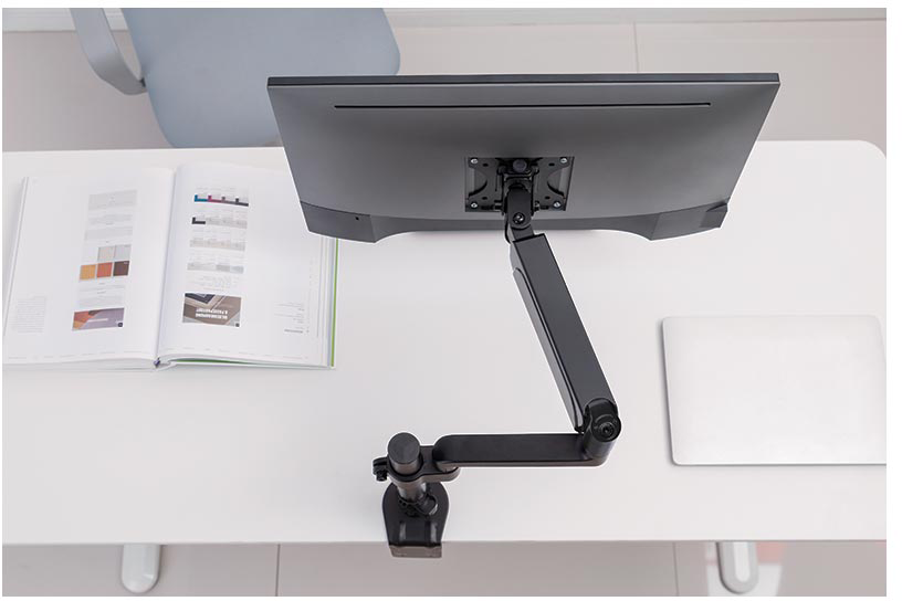 Felülnézet egy számítógépes beállításról. Egy monitor egy állítható karon, egy laptop és egy nyitott könyv.