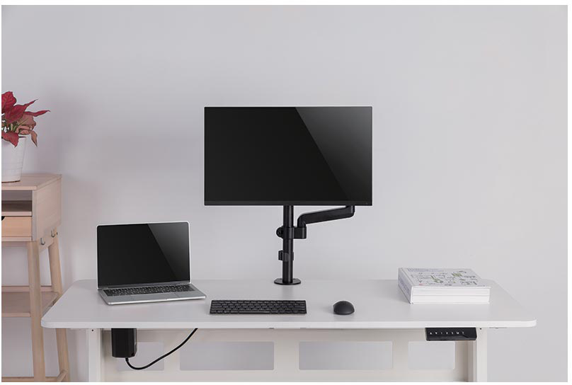 Munkahely monitorral a karon, laptop, billentyűzet, egér és asztali kiegészítők fehér asztalon.