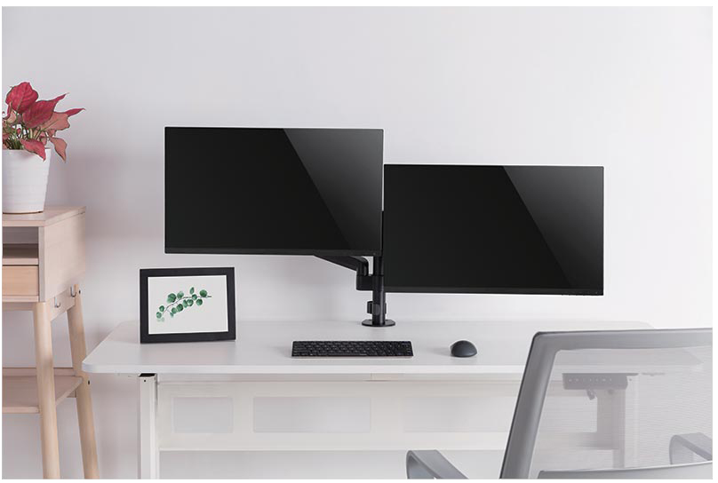 Egy asztal két fekete monitorral, billentyűzettel és egérrel. Egy növény és egy képkeret látható.