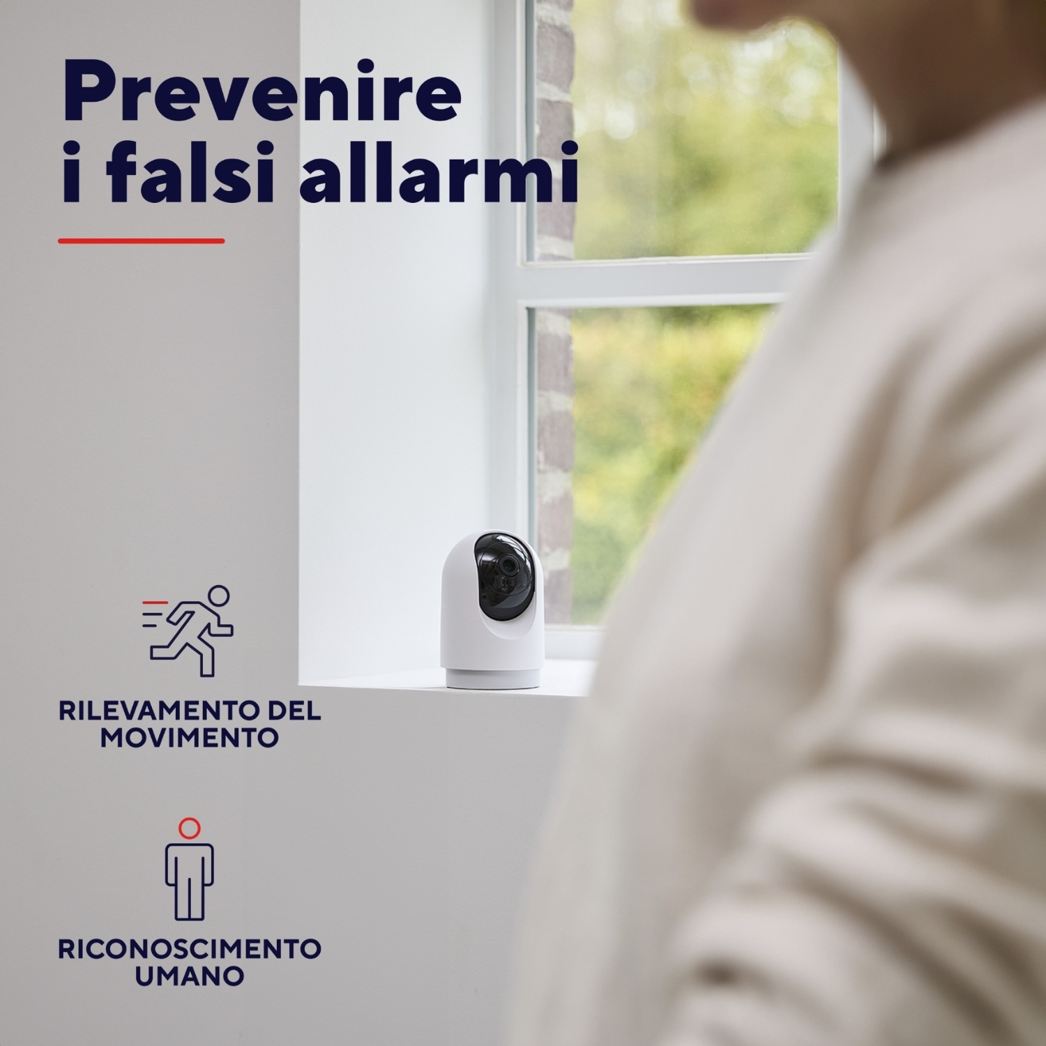 Donna con camicia arancione, in piedi vicino a una finestra. Testo e icone sulle funzioni della telecamera di sicurezza.