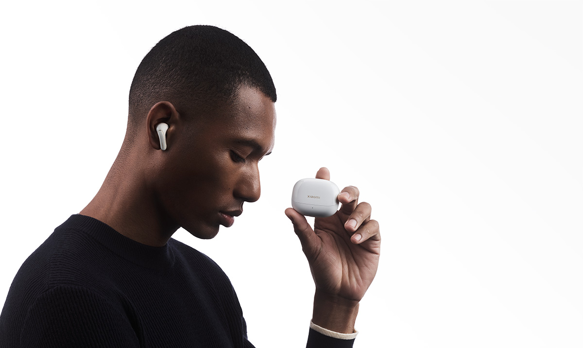 Mężczyzna trzymający białe etui na słuchawki i mający białą słuchawkę w uchu.