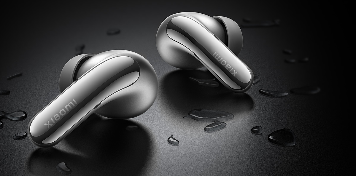 Srebrne słuchawki douszne na ciemnej powierzchni, z kroplami wody, z logo 'Xiaomi'.