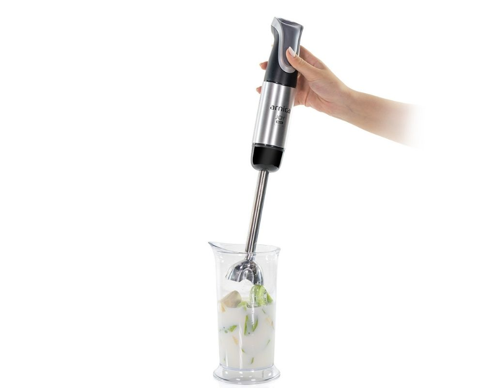 El, içinde sıvı ve yiyecek bulunan bir camın üzerinde gümüş ve siyah bir blender tutuyor.